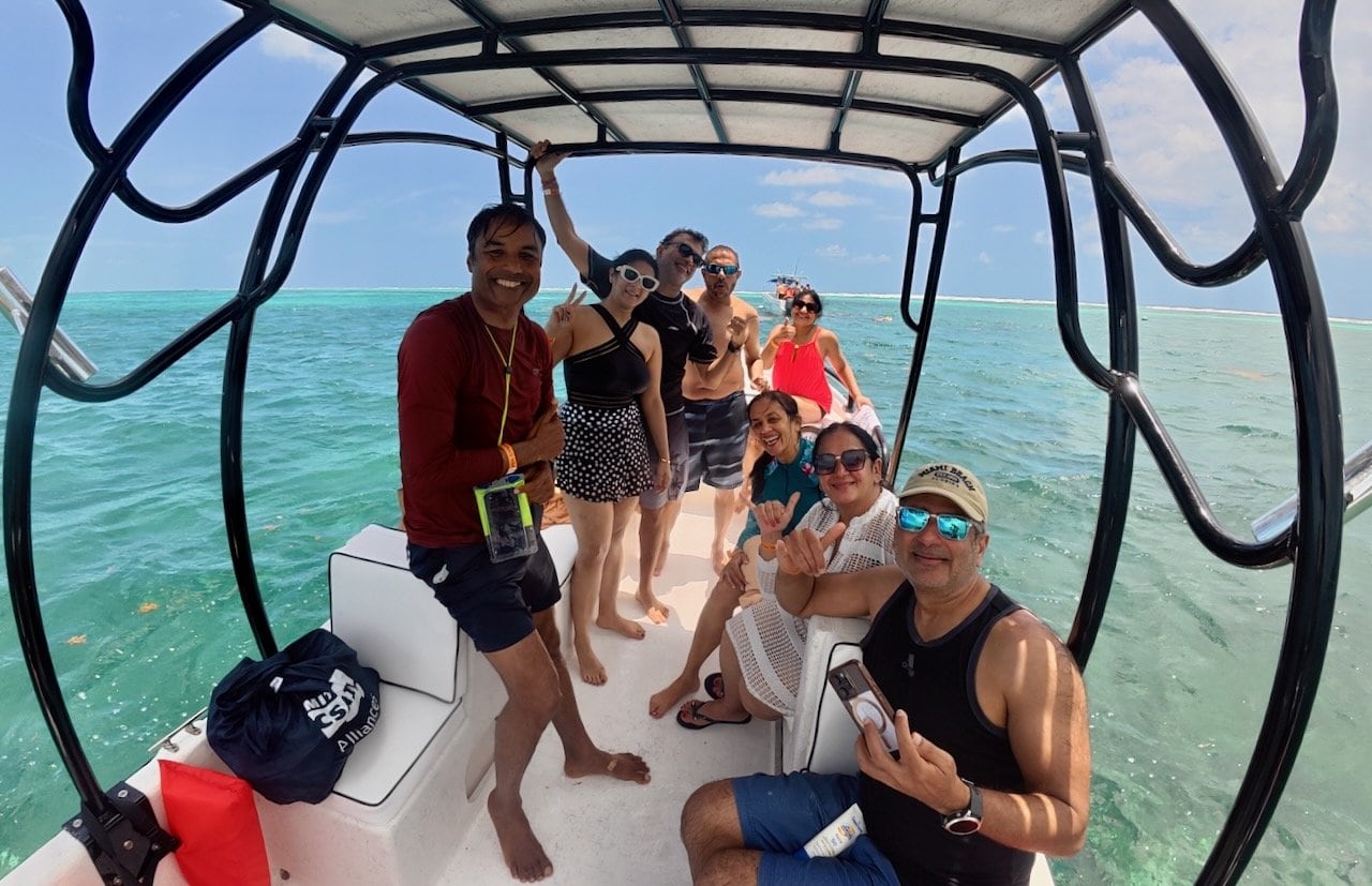 Group of eight friends on the snorkeling boat at Hol Chan Marine Reserve with the turquoise Caribbean reef behind them