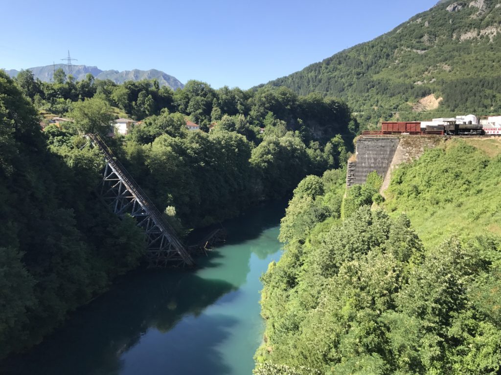 The remains of bridge in Jablanica, still lie fallen in the river. Also, on the right is an old train that may have used the bridge. I love the color of the hills and river! How stunning!