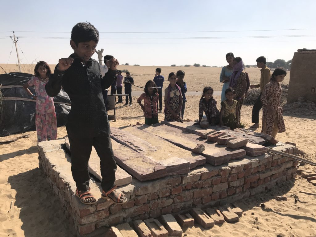 The village kids show us the underground water tank. Presumably covered to prevent evaporation and contamination. 