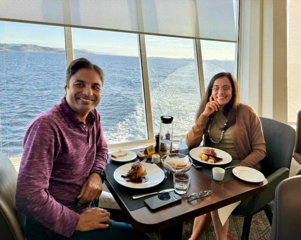 Nirmal and Jyoti dining aboard Hurtigruten cruise ship with Norwegian fjord views, plant-based meal on expedition voyage.