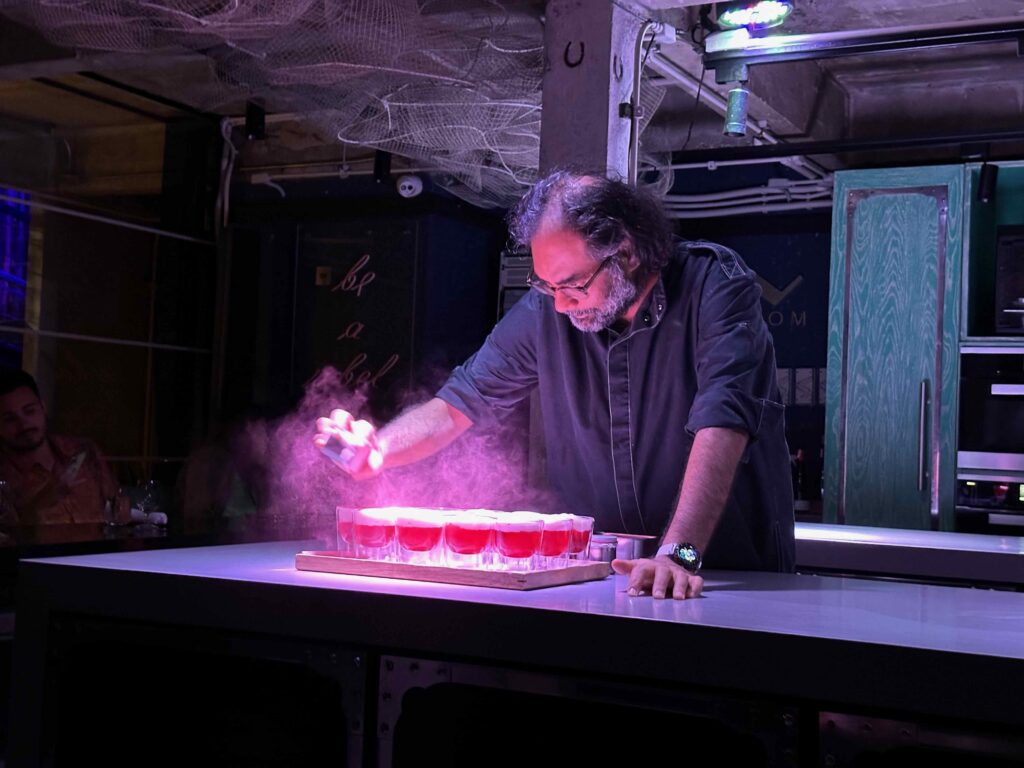 Chef Gaggan Anand adding finishing touches to glowing red drinks with smoke effects at his Michelin starred restaurant in Bangkok, private dining experience.