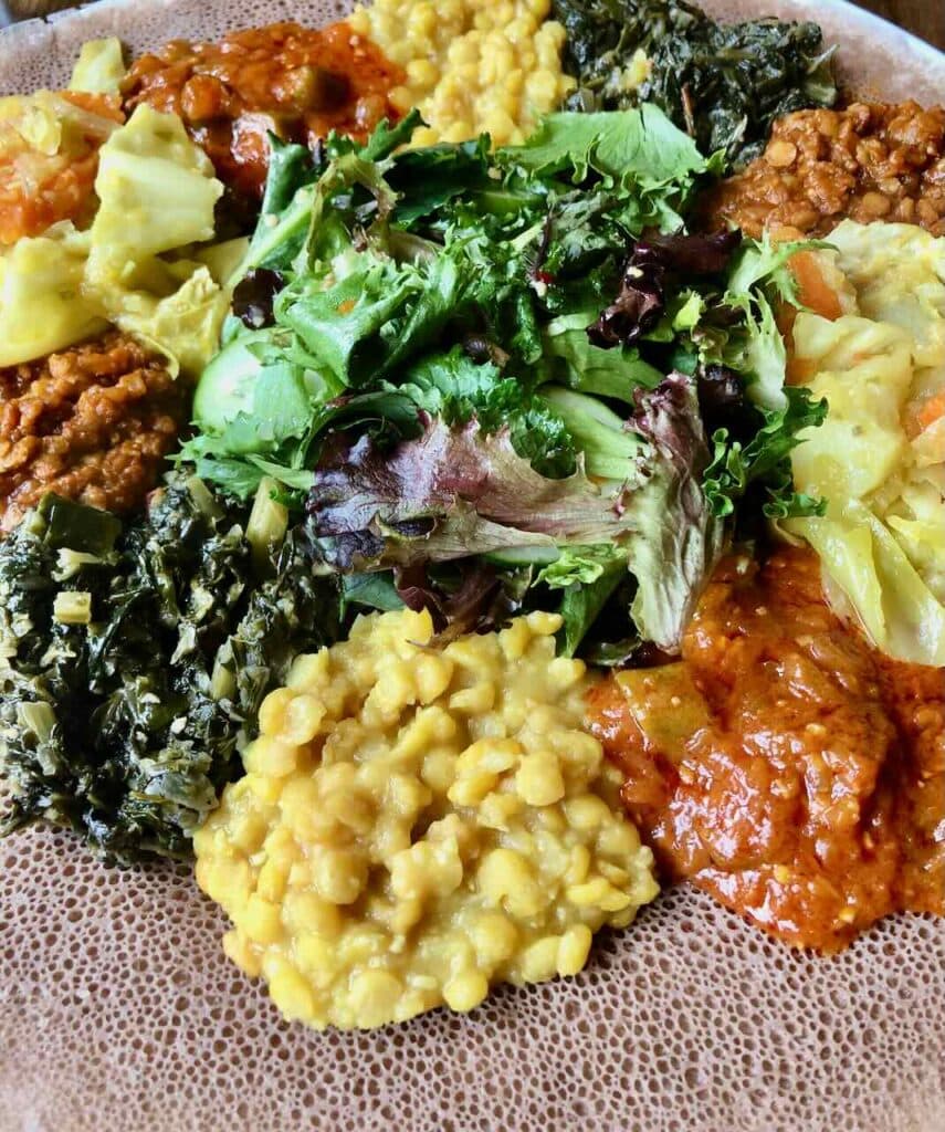 Traditional Ethiopian vegan fasting meal with injera flatbread, misir wot lentils, gomen greens, tikil gomen cabbage, and fresh salad, San Francisco