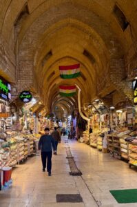 The vaulted brick arcade of the Qaysari Bazaar in Erbil with Kurdish flags hanging from the ceiling and spice and food stalls lining both sides, Iraqi Kurdistan