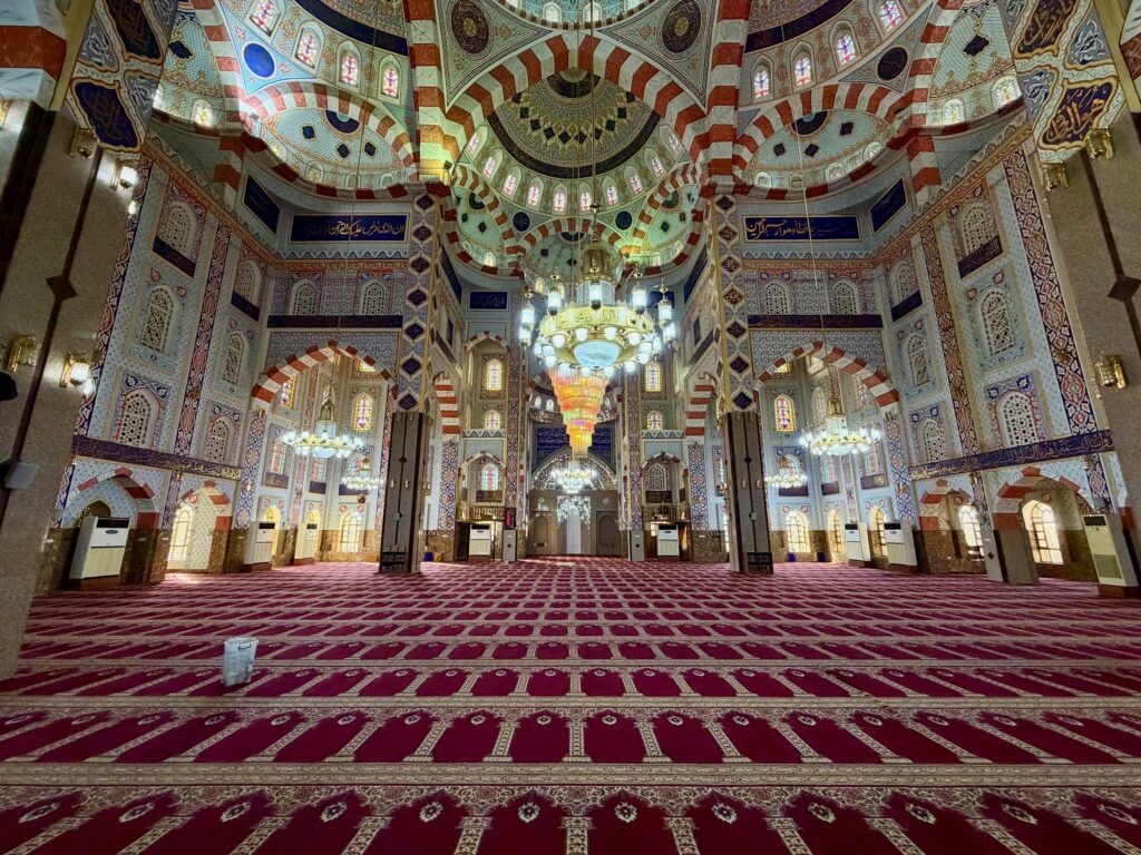 The ornate interior of Jalil Khayat Mosque in Erbil with painted dome, chandeliers and red prayer carpet, Iraqi Kurdistan