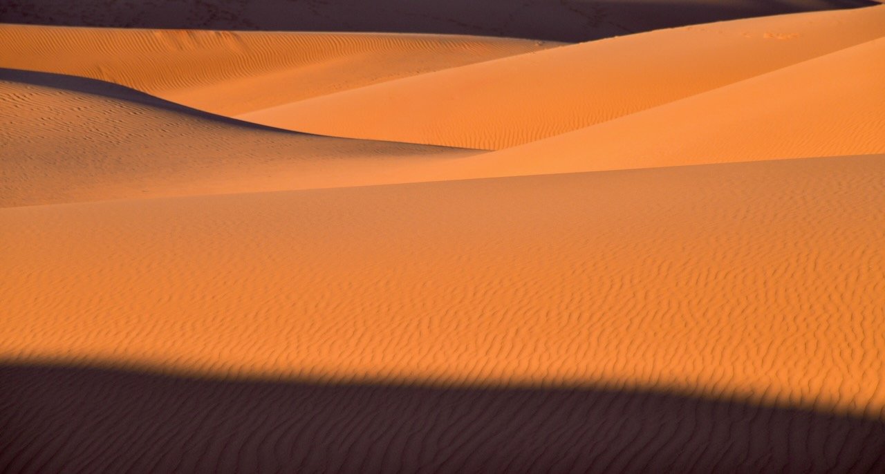 Jyoti silhouetted alone on the crest of a sand dune at Oceano Dunes at sunset with the ocean and mountain silhouettes glowing orange behind her