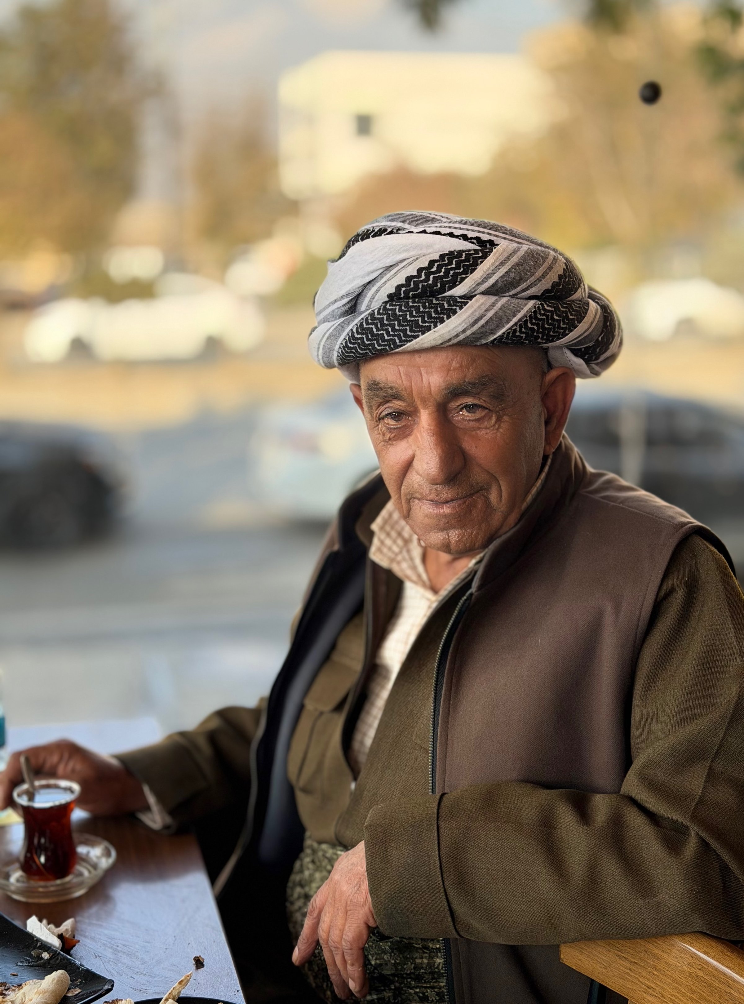 Portrait of an elderly Kurdish man in traditional striped keffiyeh holding a small glass of tea at a cafe in Erbil, Iraqi Kurdistan
