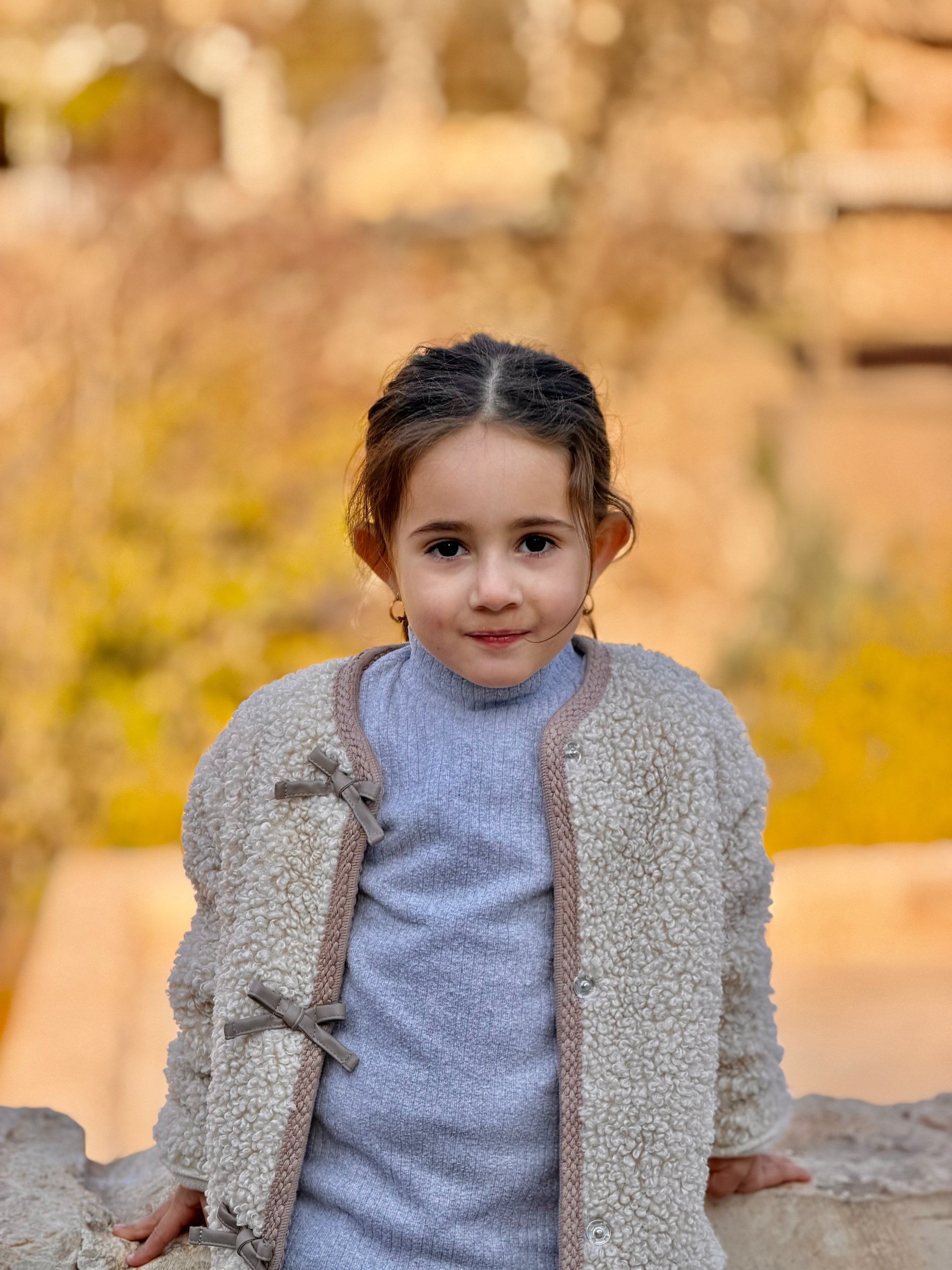 Portrait of a young Kurdish girl with braided hair sitting against golden autumn bokeh at Lalish, Iraqi Kurdistan