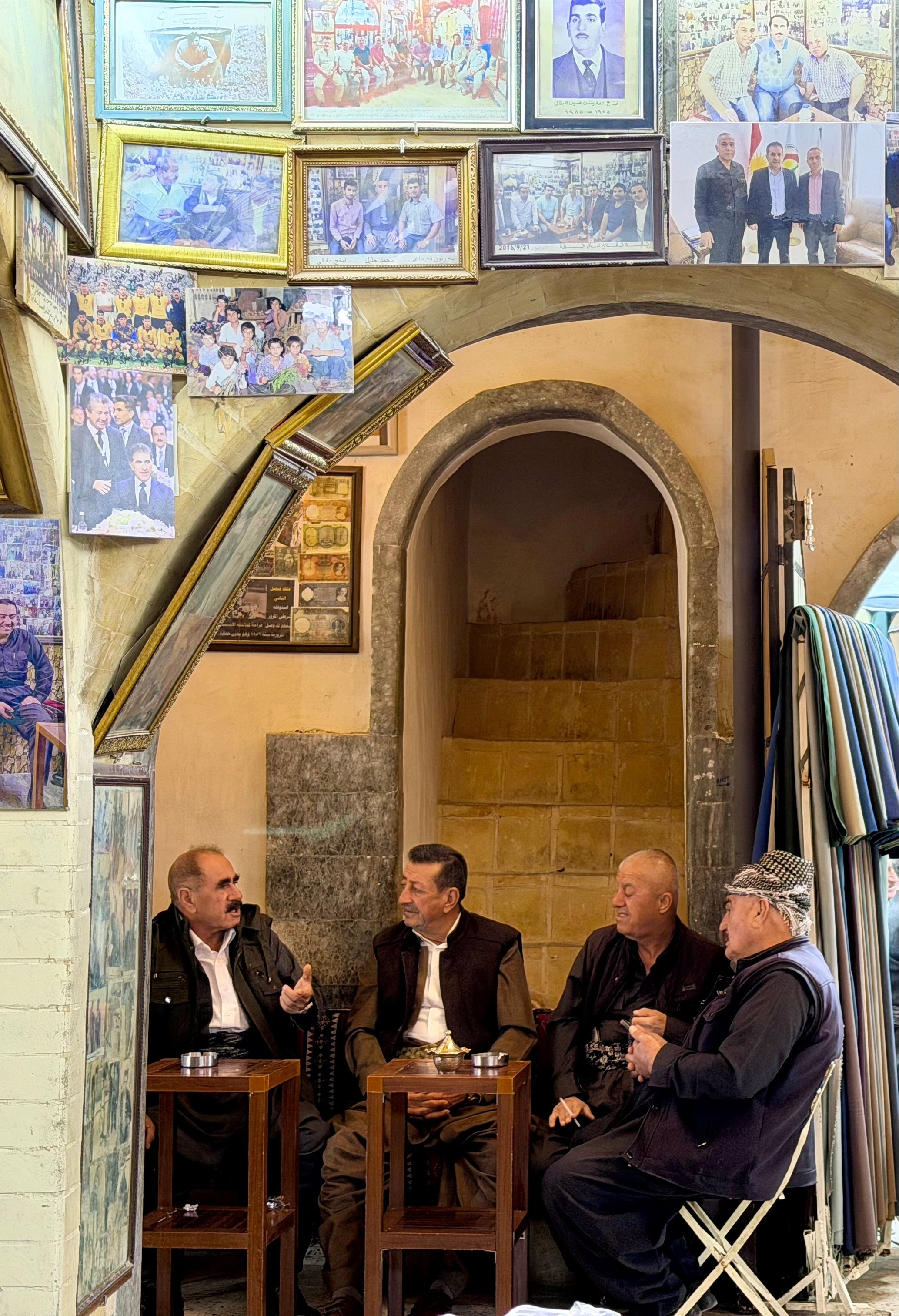 Kurdish men drinking tea in the historic Erbil Citadel bazaar surrounded by framed photographs on the walls, Iraqi Kurdistan