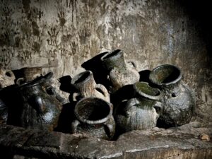 Ancient clay oil pots stacked against a stone wall covered in generations of handprints left by Yazidi pilgrims at the Lalish temple, Iraqi Kurdistan