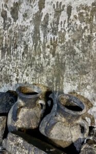 Wide view of the Lalish Yazidi temple complex with conical shrines rising above stone walls and the wooded mountain valley behind, Iraqi Kurdistan