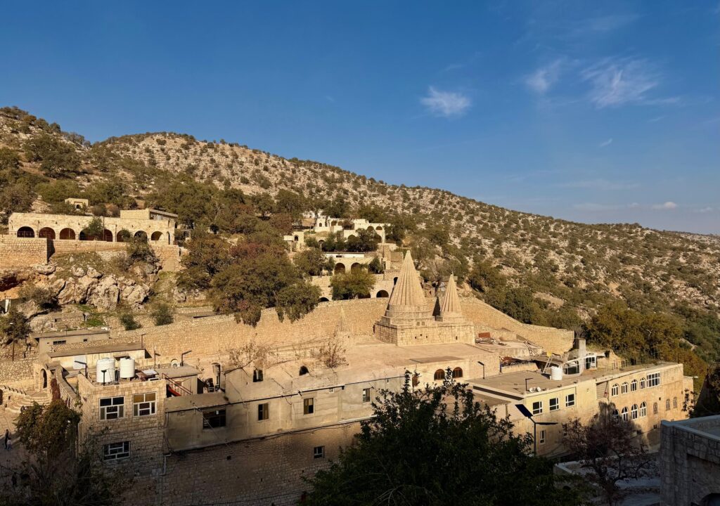 Stone-vaulted sanctuary corridor at the Lalish Yazidi temple hung with colourful silk drapes in green, red, purple and yellow over sacred shrines, Iraqi Kurdistan