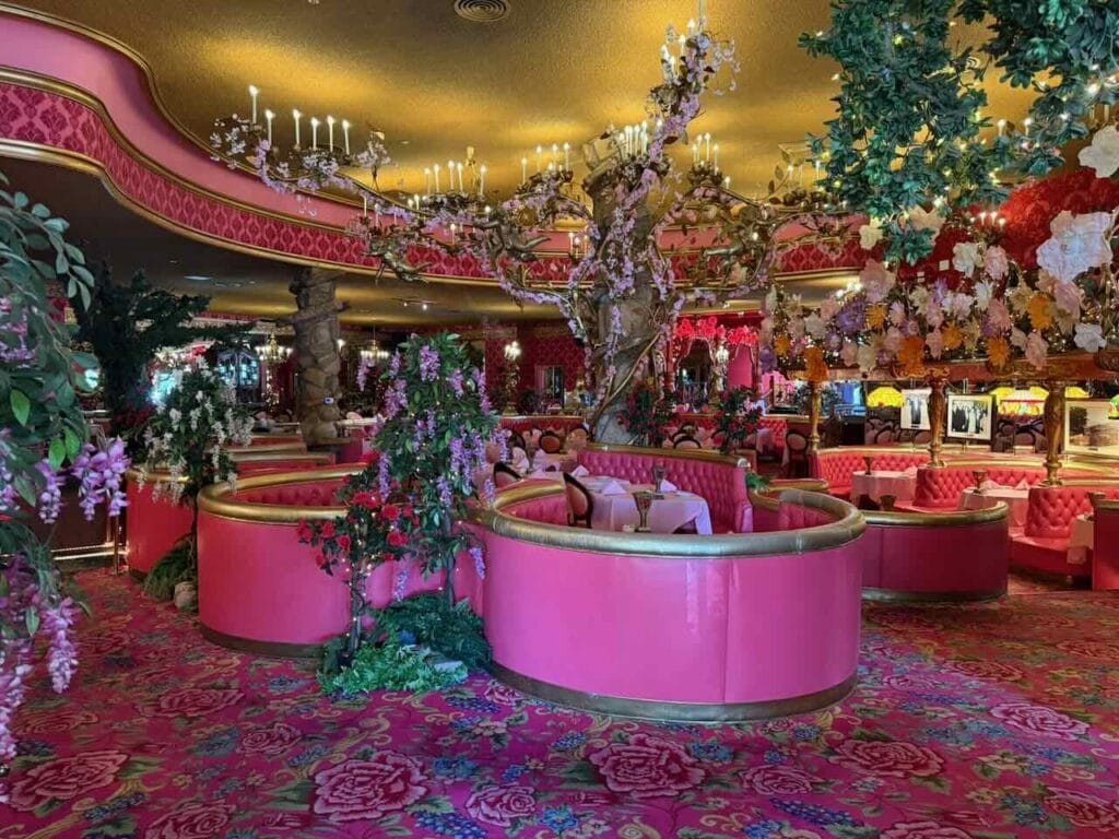 The extravagant pink and gold dining room of the Madonna Inn in San Luis Obispo with circular pink booths flowering trees chandeliers and floral carpeting