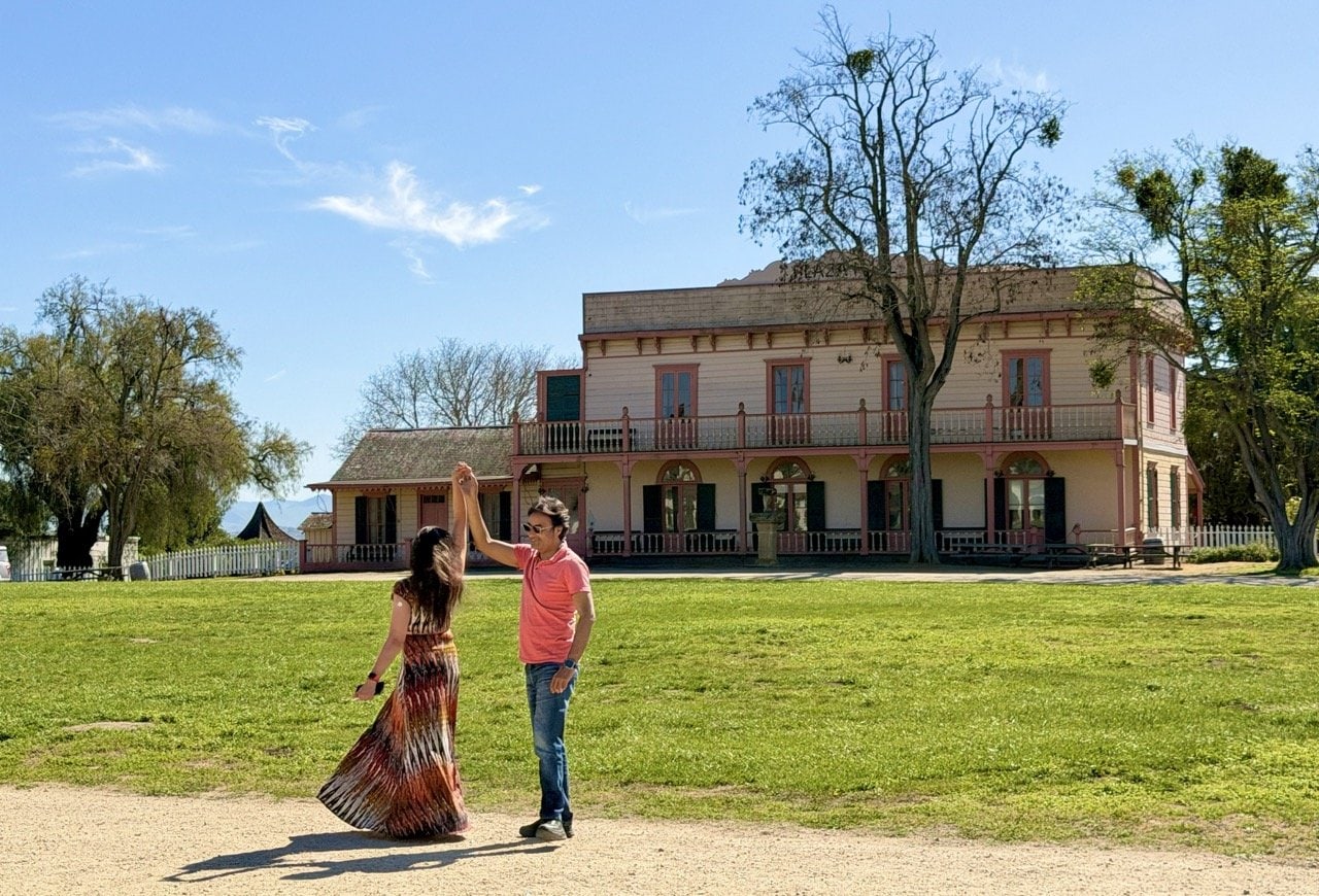 Nirmal and Jyoti dancing on the historic plaza in front of the pink Plaza Hotel building at Mission San Juan Bautista