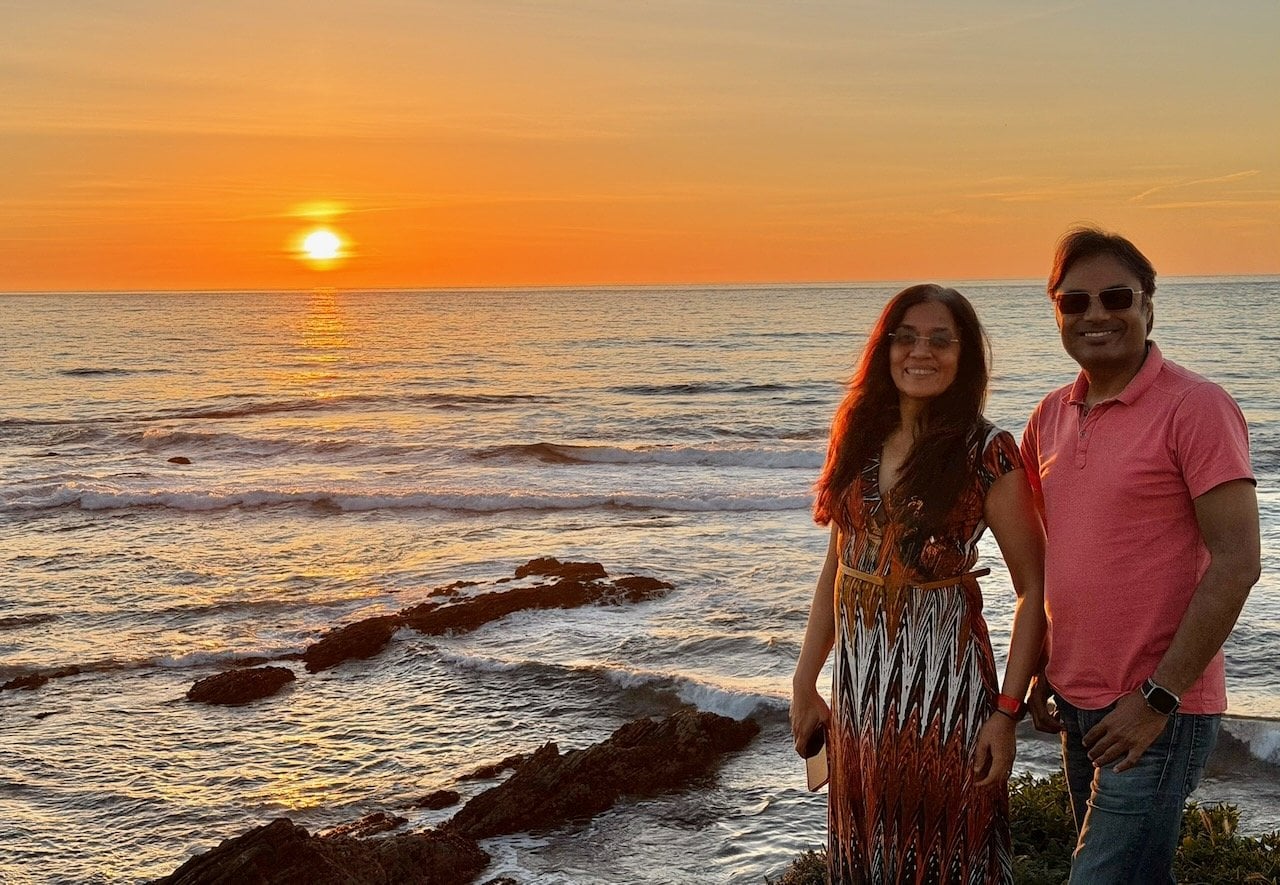 Nirmal and Jyoti standing together on the sea cliffs at Montana de Oro State Park with the rugged coastline and green hills behind
