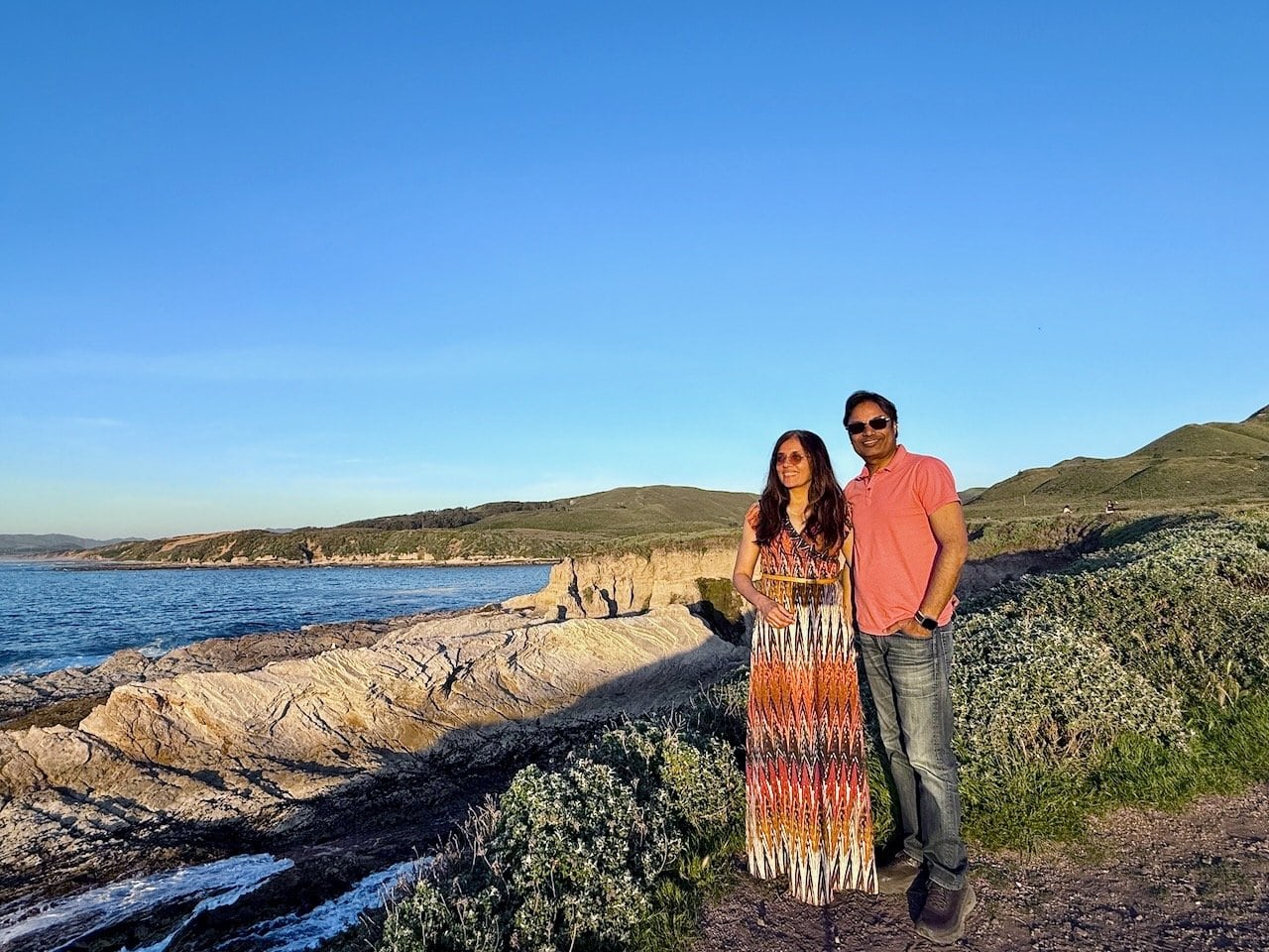 Jyoti and Nirmal at sunset on the rocky bluffs at Montana de Oro State Park with the Pacific Ocean glowing orange behind them