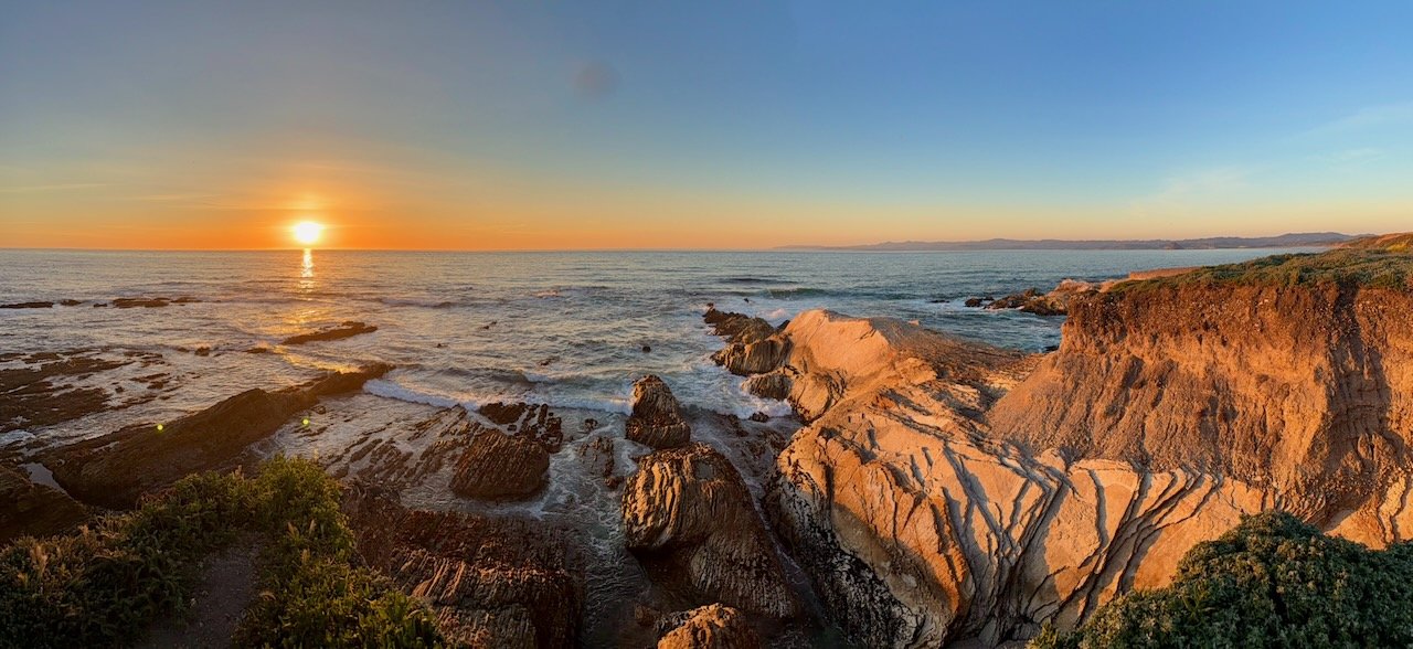 Panoramic sunset view over the sea cliffs at Montana de Oro State Park with layered golden rocks and the Pacific Ocean stretching to the horizon