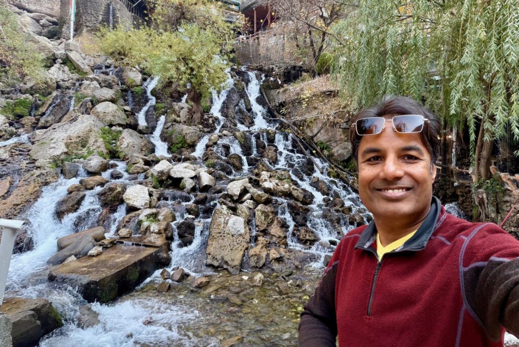 Nirmal taking a selfie at Bekhal Waterfall near Rawanduz with the waterfall cascading behind him, Iraqi Kurdistan