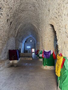 Nirmal walking through the stone-vaulted underground oil chamber at the Lalish Yazidi temple, lined with rows of sacred clay pots, Iraqi Kurdistan