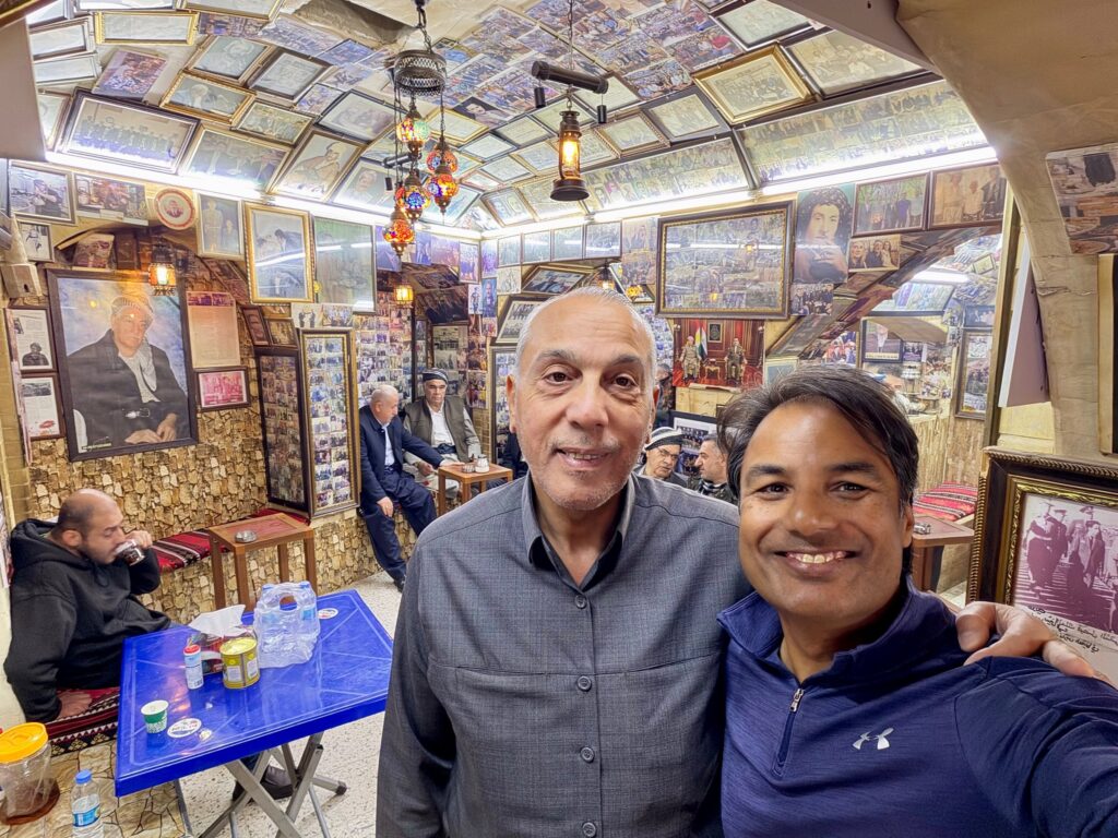 Nirmal taking a selfie with a local man inside a famous historic tea house in Erbil with every wall and ceiling covered in framed photographs and portraits, Iraqi Kurdistan