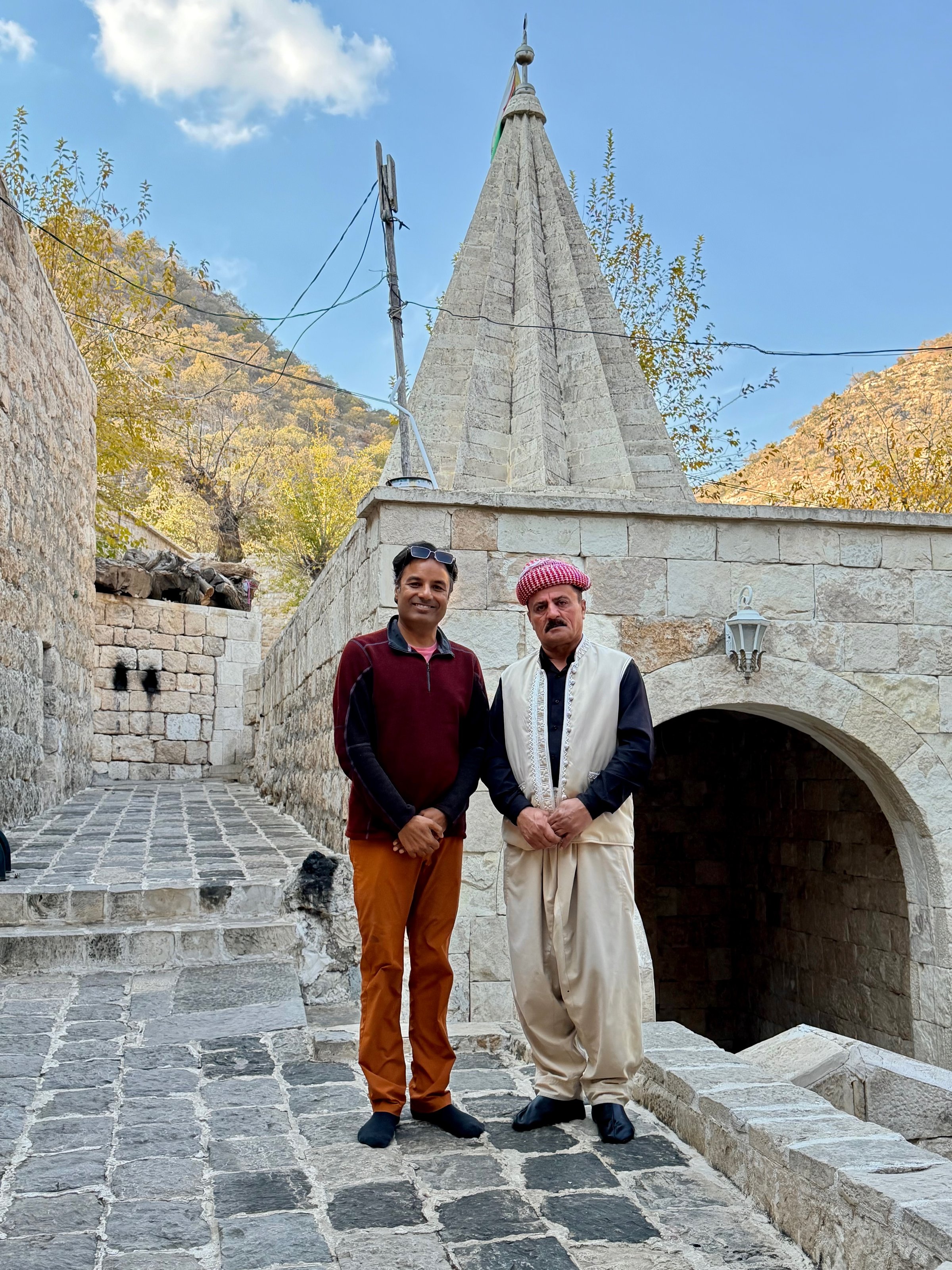 Nirmal with a Yazidi elder in front of the conical shrines at the Lalish temple complex, Iraqi Kurdistan