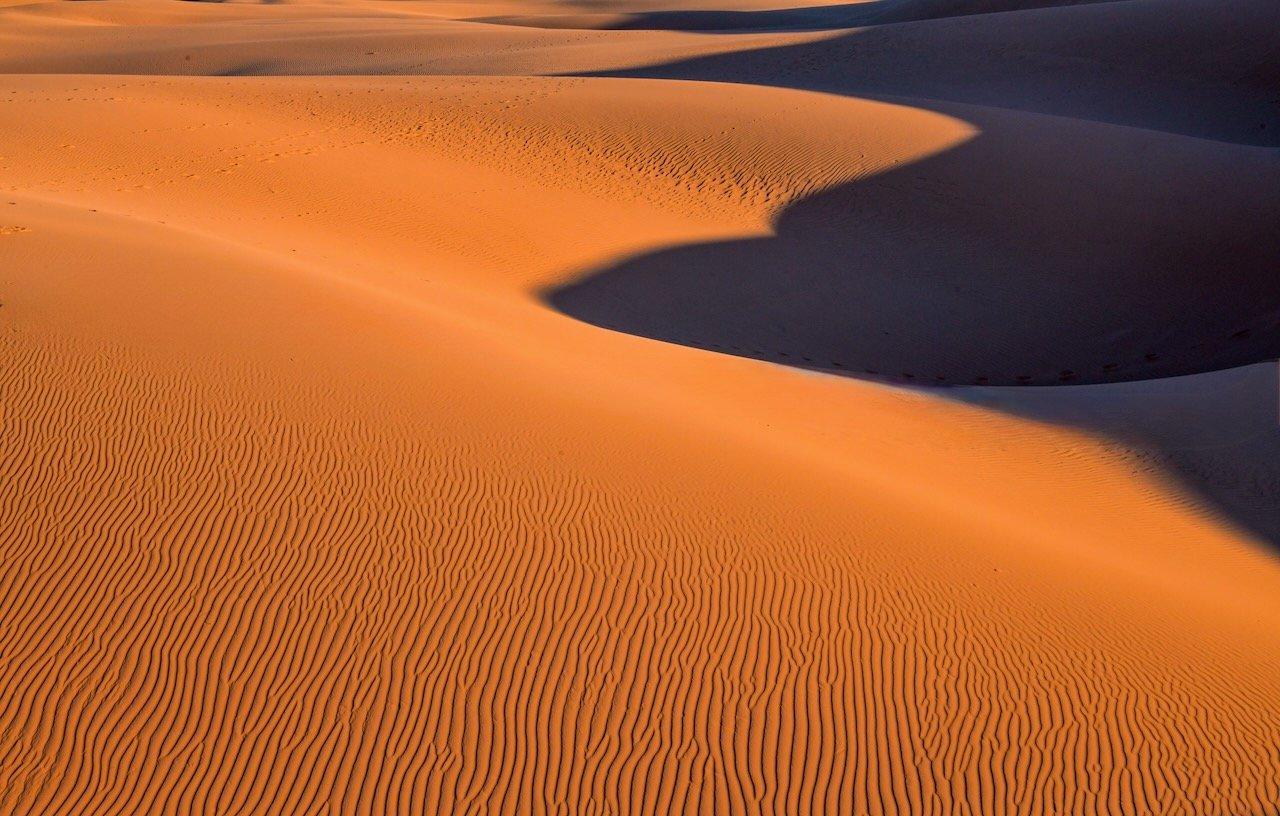Abstract close-up of orange sand dune ripples and shadow patterns at Oceano Dunes in late afternoon light