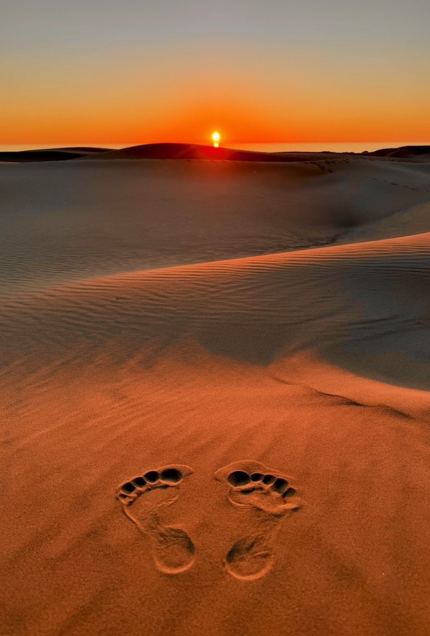 Vast golden sand dunes at Oceano at sunset with the Pacific Ocean visible on the horizon and silhouetted mountains in the distance