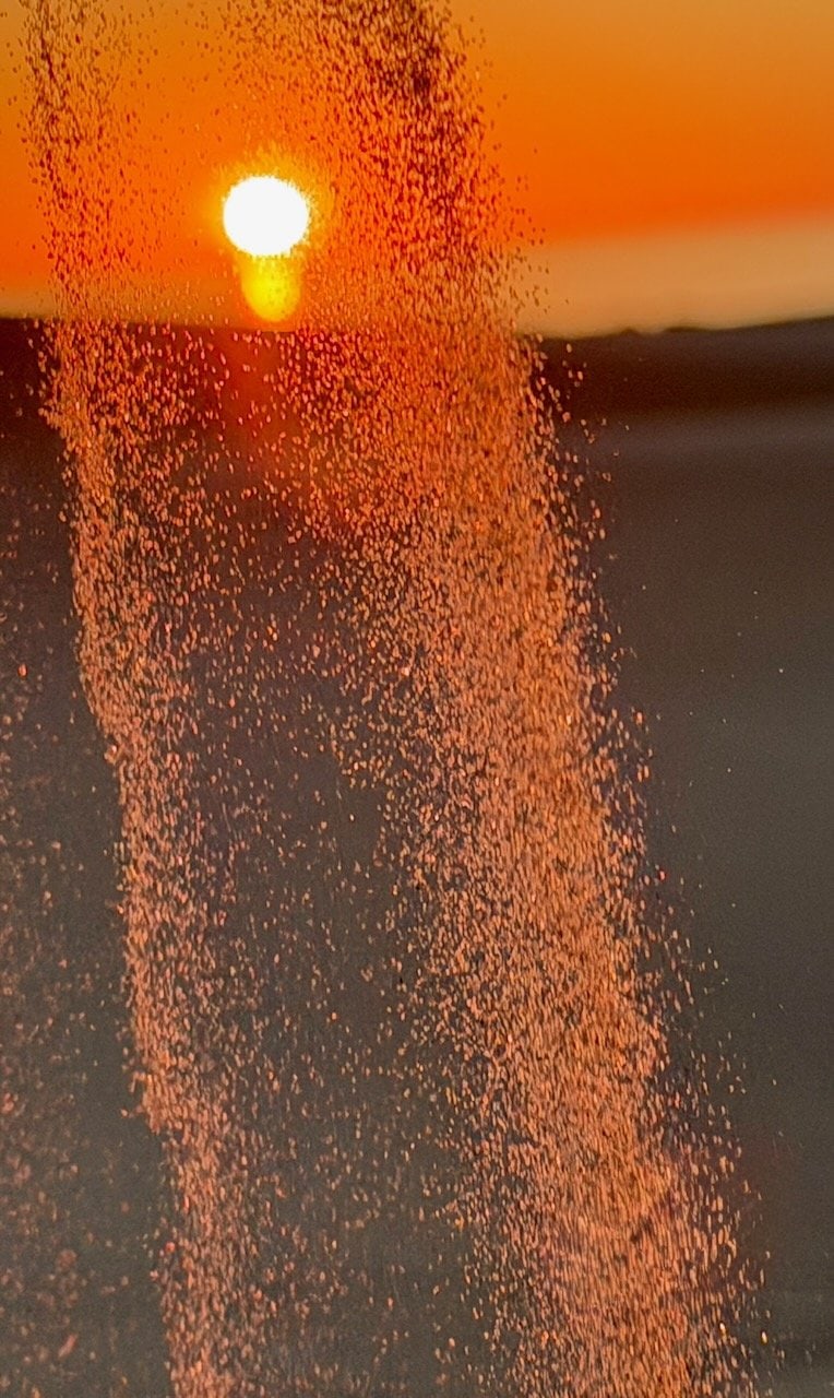 Sand cascading off the crest of a dune at Oceano at sunset backlit by the setting sun creating a sparkling curtain of airborne sand particles