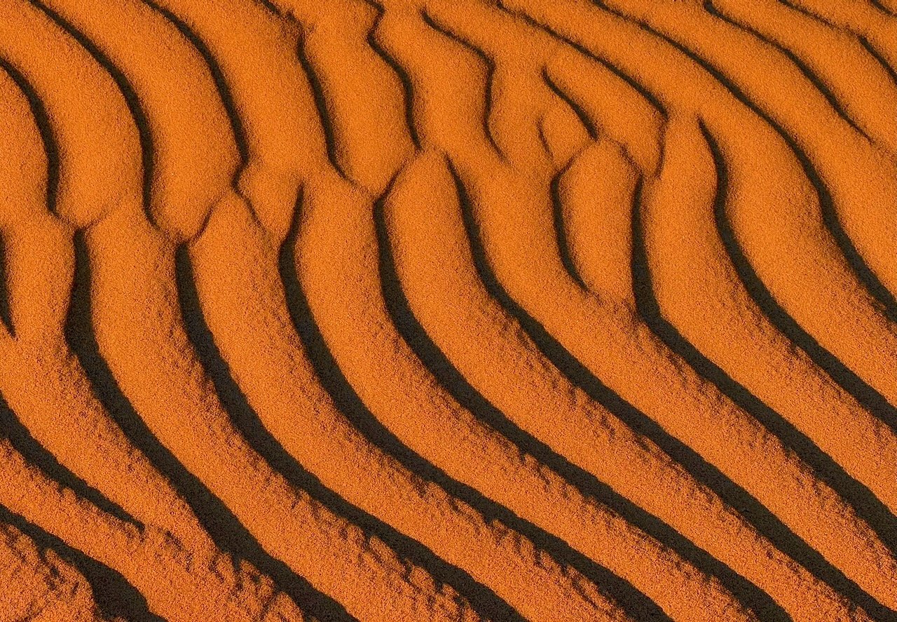 Close-up abstract photograph of orange and deep brown sand dune ripple patterns at Oceano Dunes in raking light