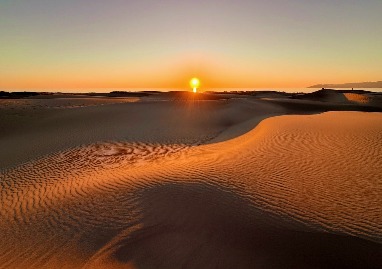 Golden sand dunes at Oceano at sunset with the sun setting behind the dune crest and footprints in the foreground sand