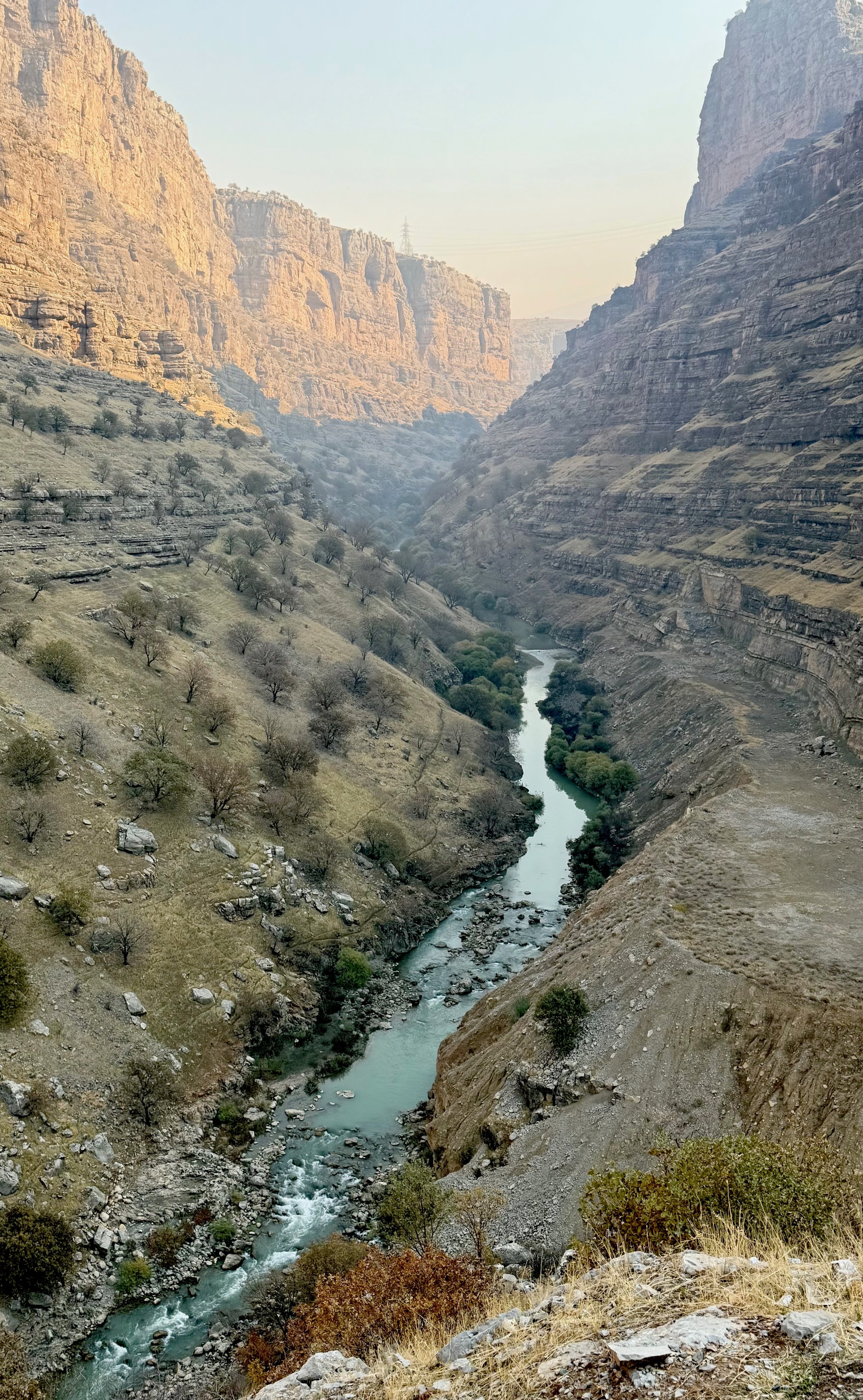 Wide aerial view of Rawanduz Canyon with a turquoise river winding between towering limestone cliffs and terraced hillsides, Iraqi Kurdistan