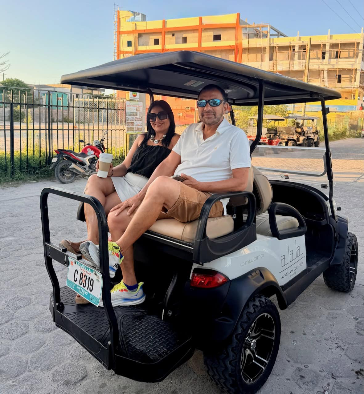Jaya and Srini are seated in an Alaia Belize Autograph Collection golf cart on a street in San Pedro, Ambergris Caye, Belize