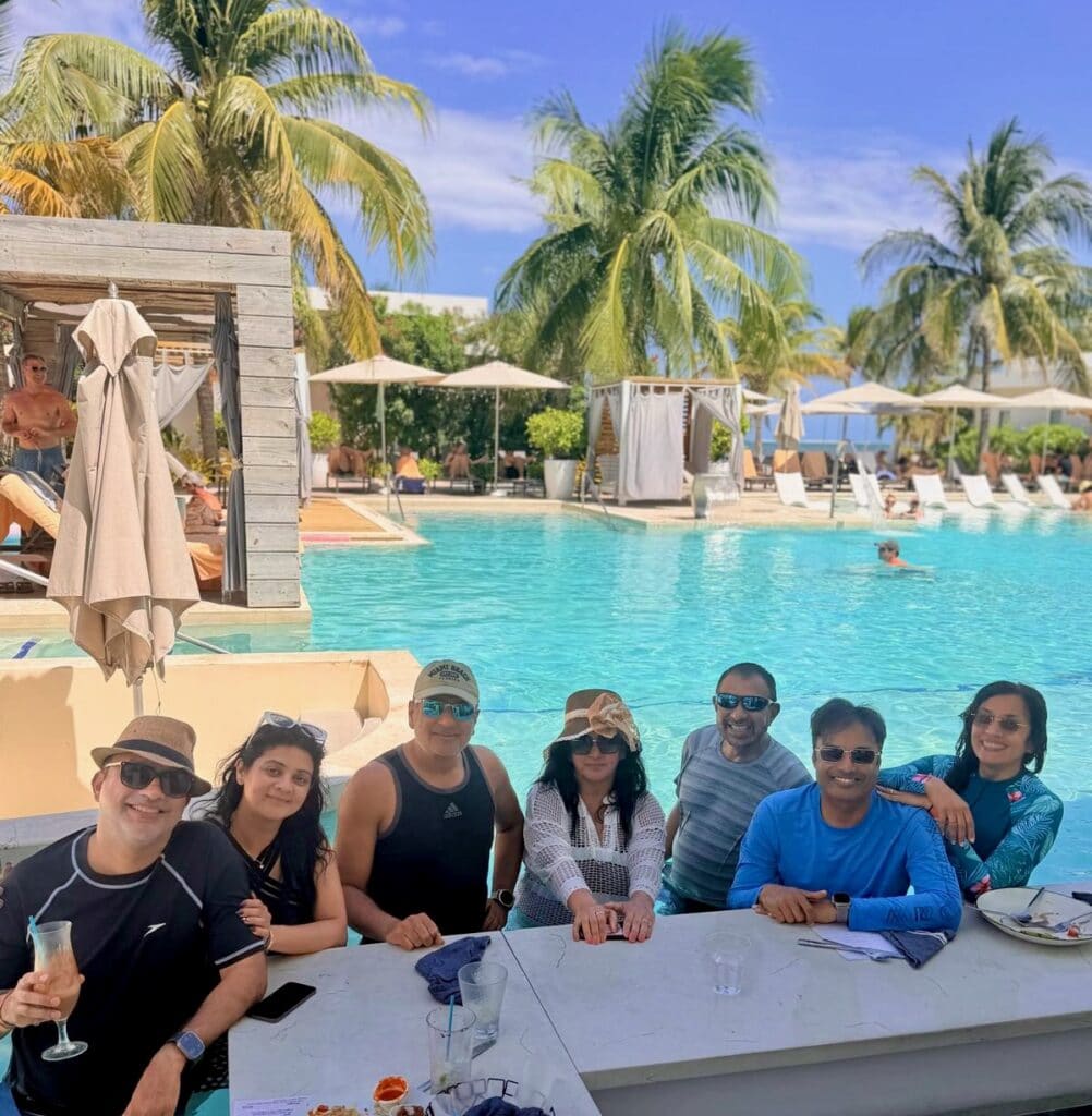 Group of seven friends having a casual lunch poolside bar at Alaia Belize, with the pool and palm trees visible behind them