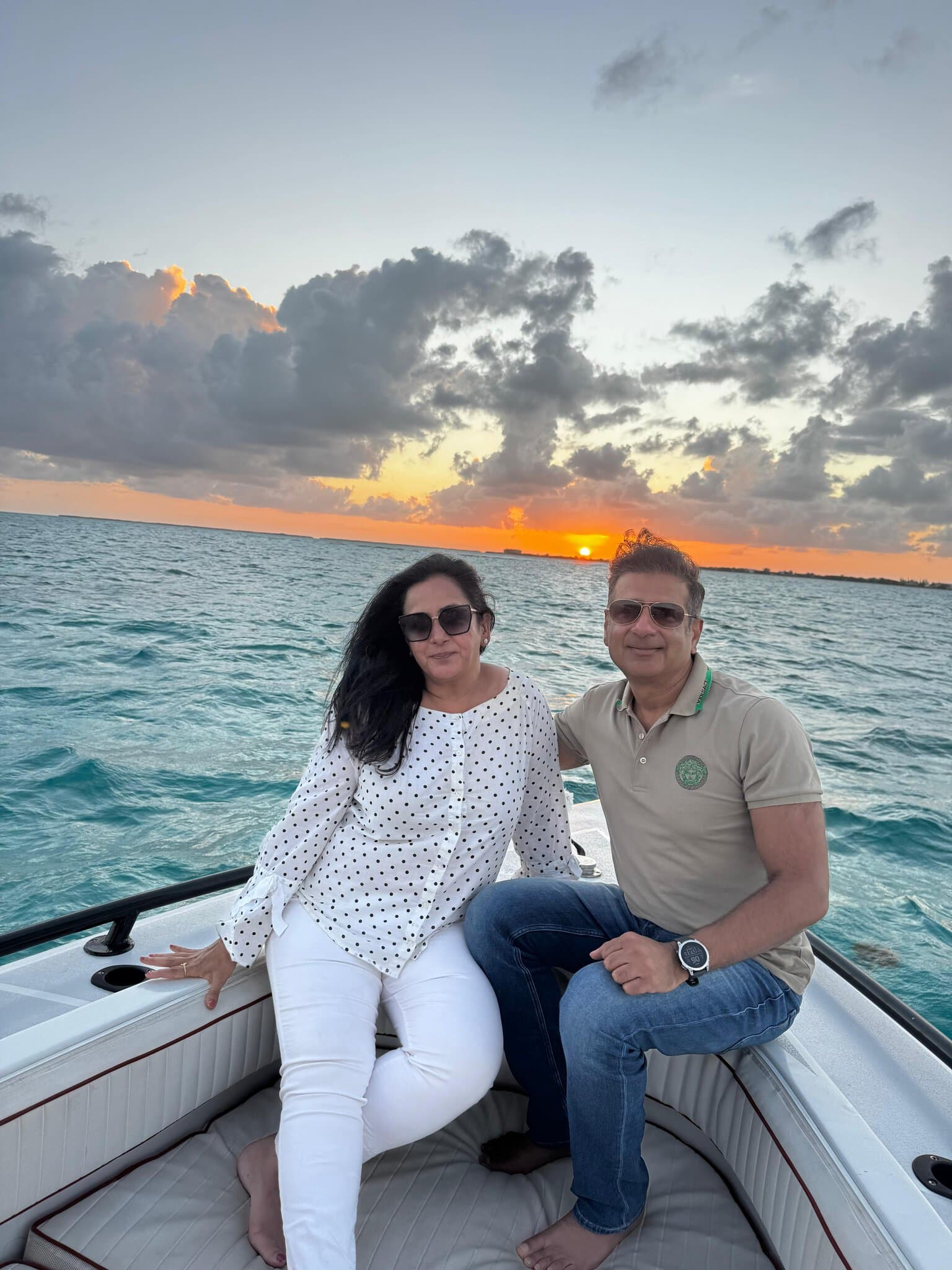 Mona and Sunit sitting on the bow of a boat during a sunset cruise in San Pedro, Belize, with orange skies over the Caribbean Sea