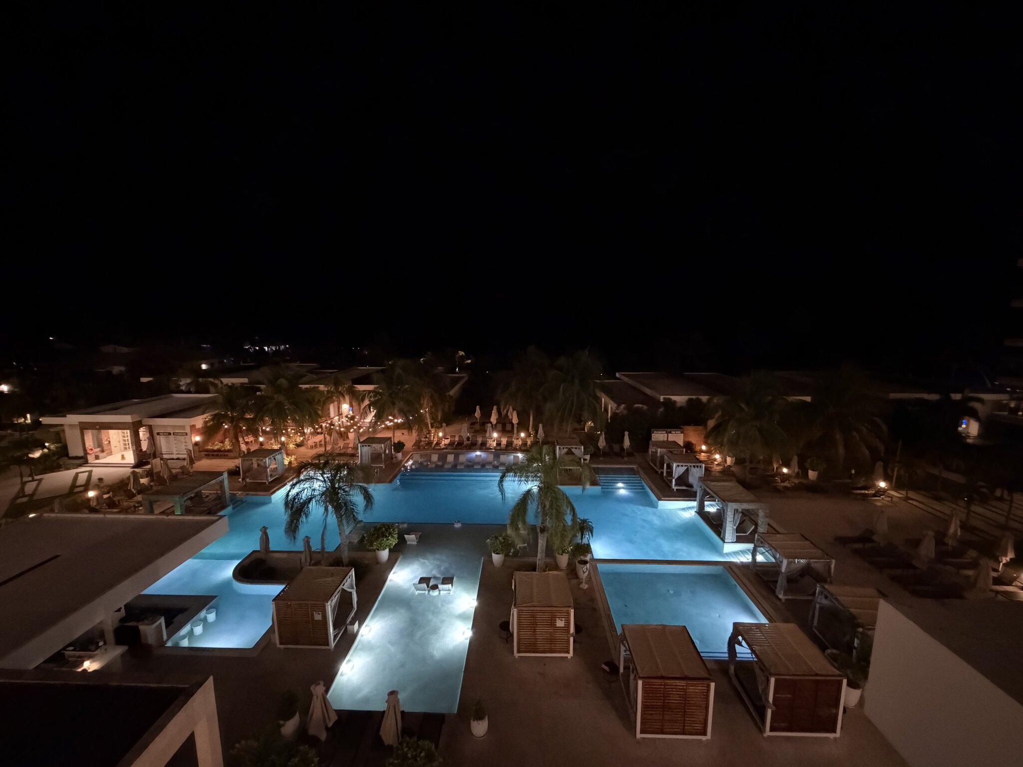 Bird's-eye view of the three illuminated pools at Alaia Belize Marriott from an upper floor at night