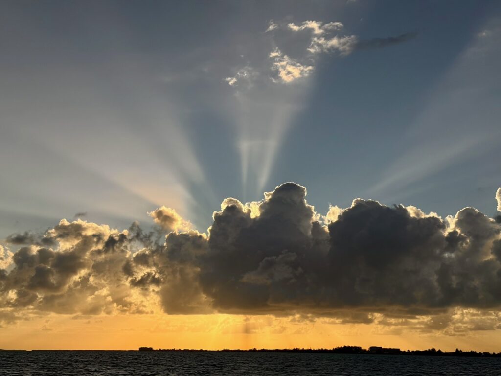 Dramatic crepuscular rays fanning above a large storm cloud at sunset over the Caribbean Sea near San Pedro, Belize, with an island silhouette on the horizon.