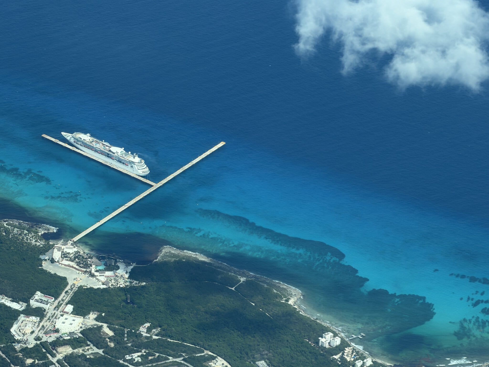 Aerial view of a cruise ship docked at the long pier in Mahahual, Mexico, surrounded by turquoise Caribbean water