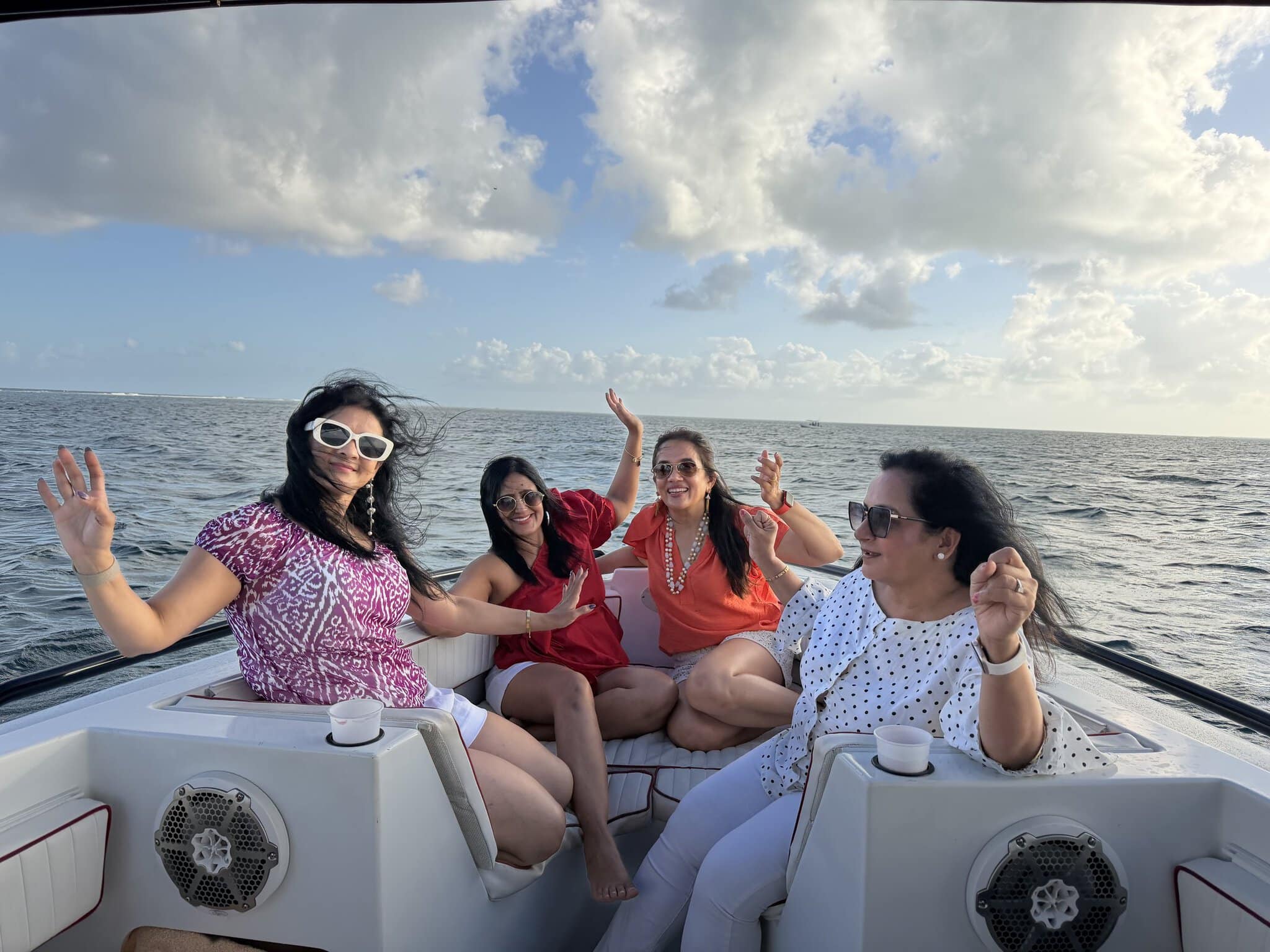 Four women dancing and waving on the bow of a sunset cruise boat on the Caribbean Sea near San Pedro