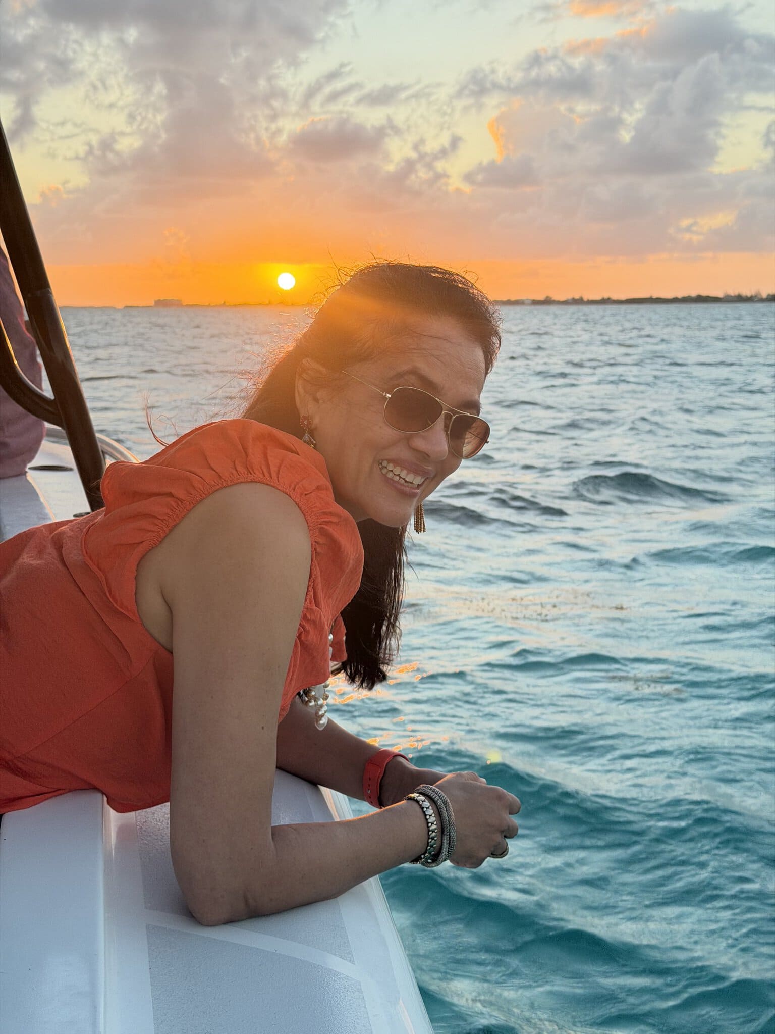Jyoti leaning over the bow of the sunset cruise boat with a brilliant orange Caribbean sunset directly behind her