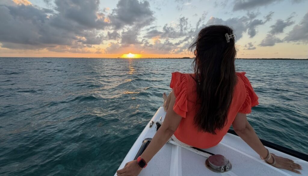 Jyoti sitting on the bow of a chartered sunset cruise boat, looking toward the setting sun over the Caribbean Sea near San Pedro, Belize