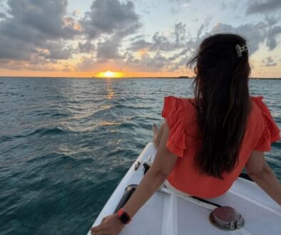 Jyoti sitting on the bow of a chartered sunset cruise boat, looking toward the setting sun over the Caribbean Sea near San Pedro, Belize