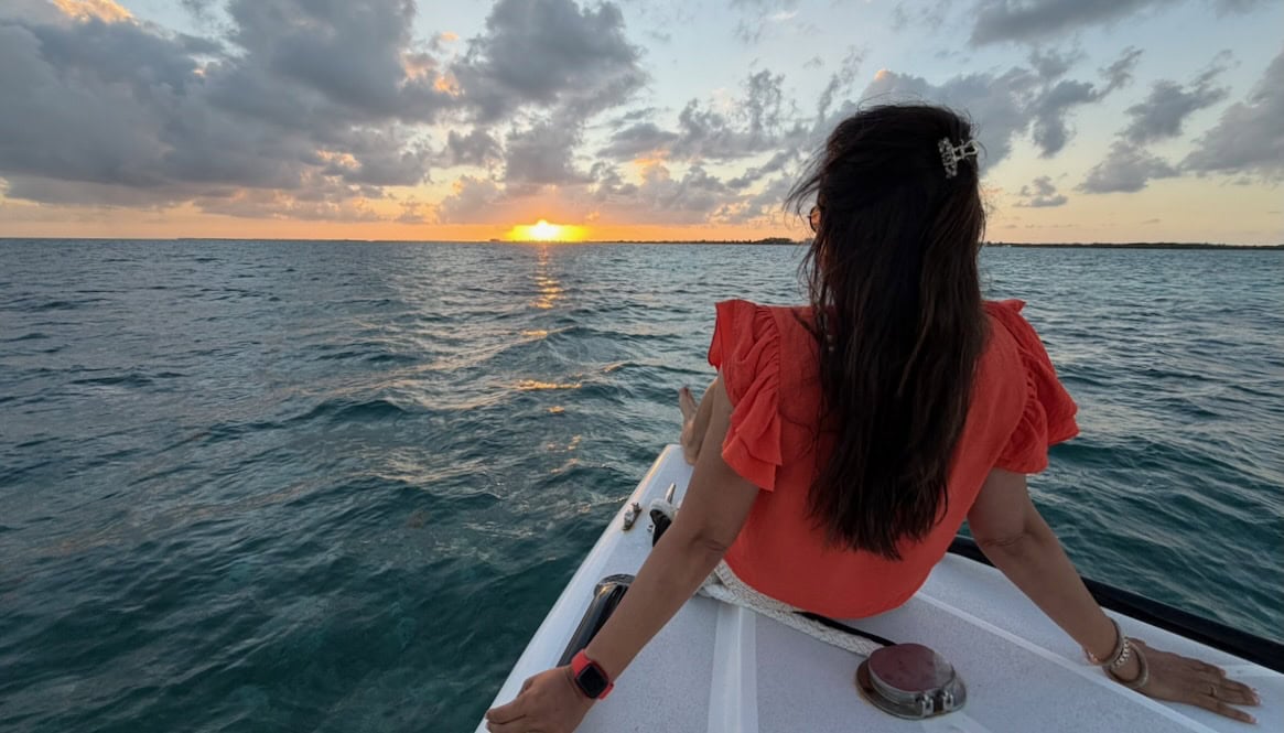 Jyoti sitting on the bow of a chartered sunset cruise boat, looking toward the setting sun over the Caribbean Sea near San Pedro, Belize