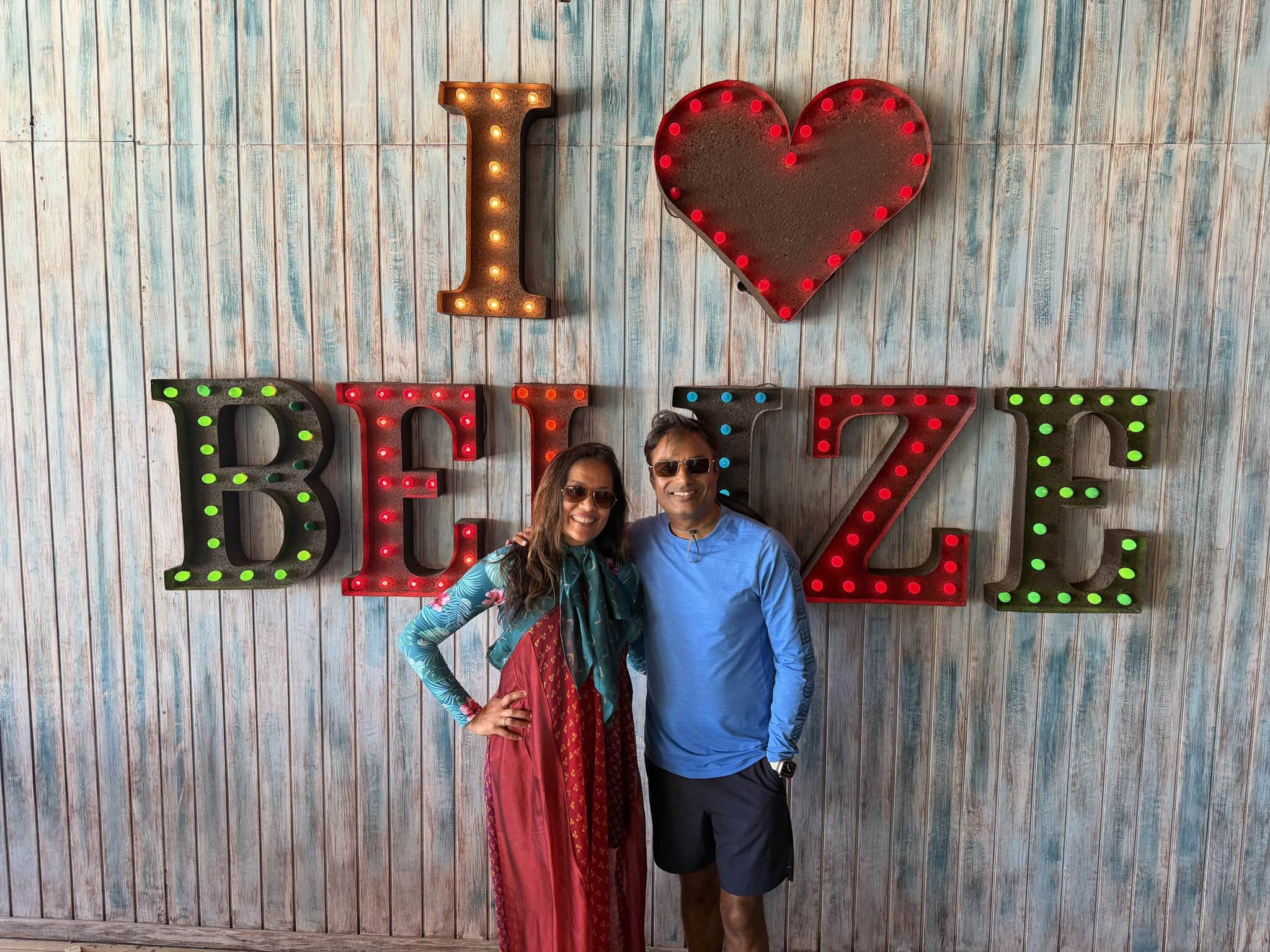 Nirmal and Jyoti in front of the illuminated I Love Belize neon marquee sign at Blue Water Grill, San Pedro