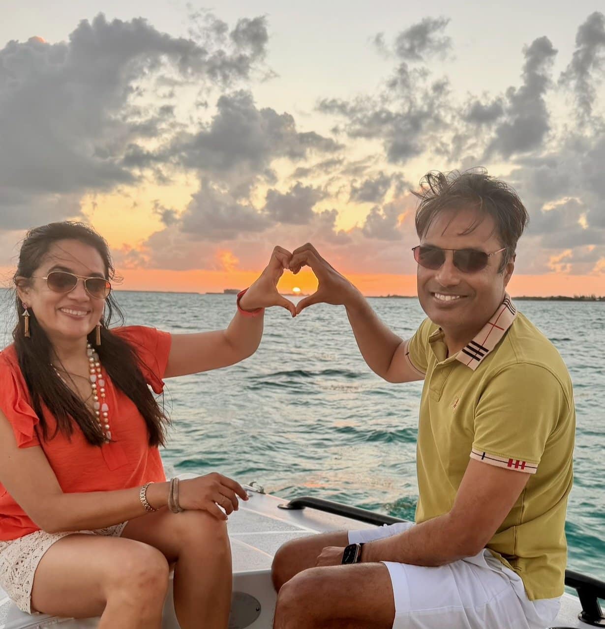Nirmal and Jyoti on a sunset cruise in San Pedro Belize, framing the setting sun in a heart shape with their hands