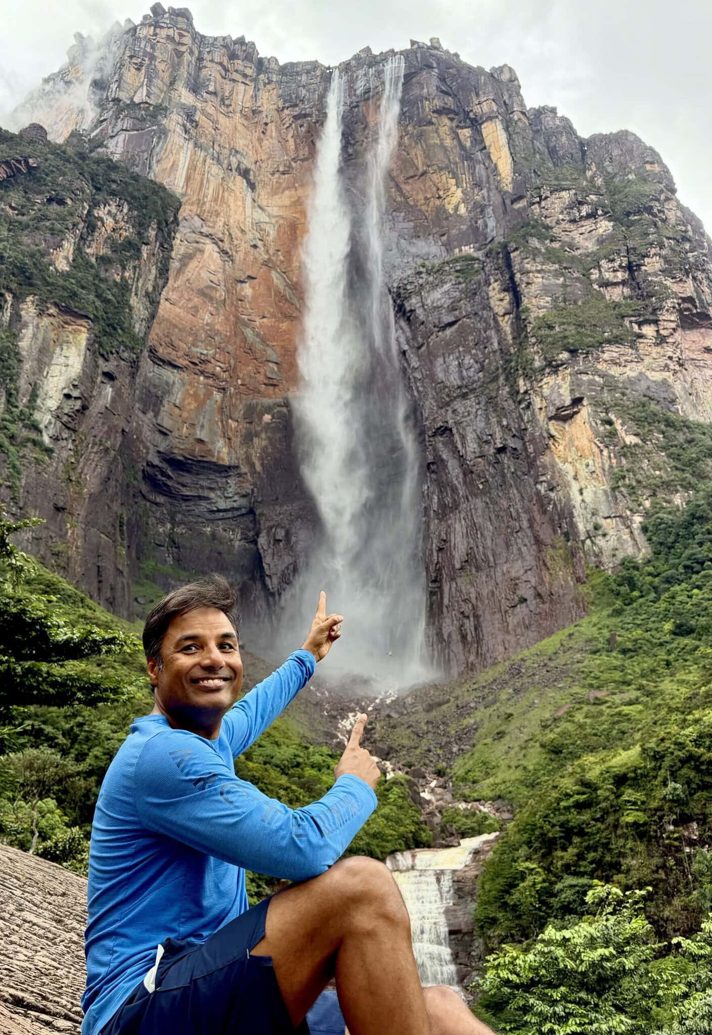 Man pointing at Angel Falls dropping nearly one kilometer down Auyan Tepui cliff face in Venezuela