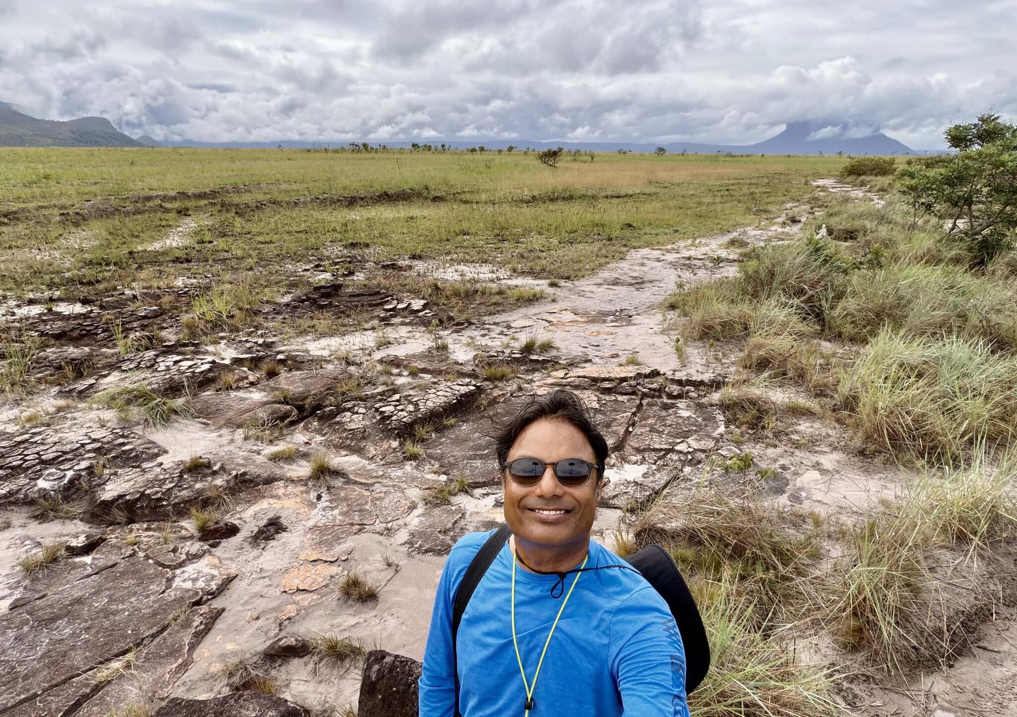 Man in blue shirt smiling on rocky Gran Sabana terrain with tepui mountains and vast savanna behind