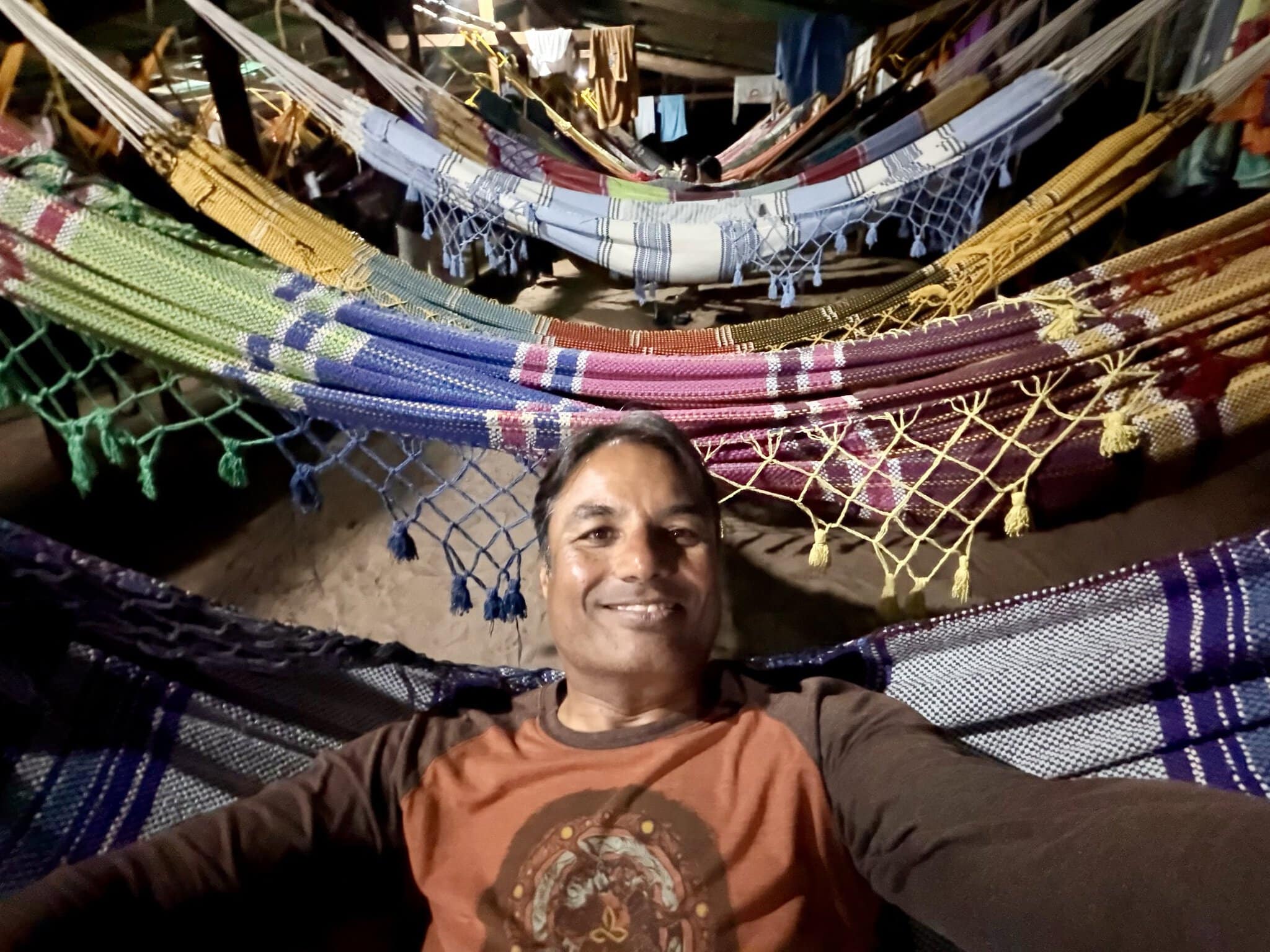 Traveler lying among colorful woven hammocks at jungle camp near Angel Falls, Venezuela at night