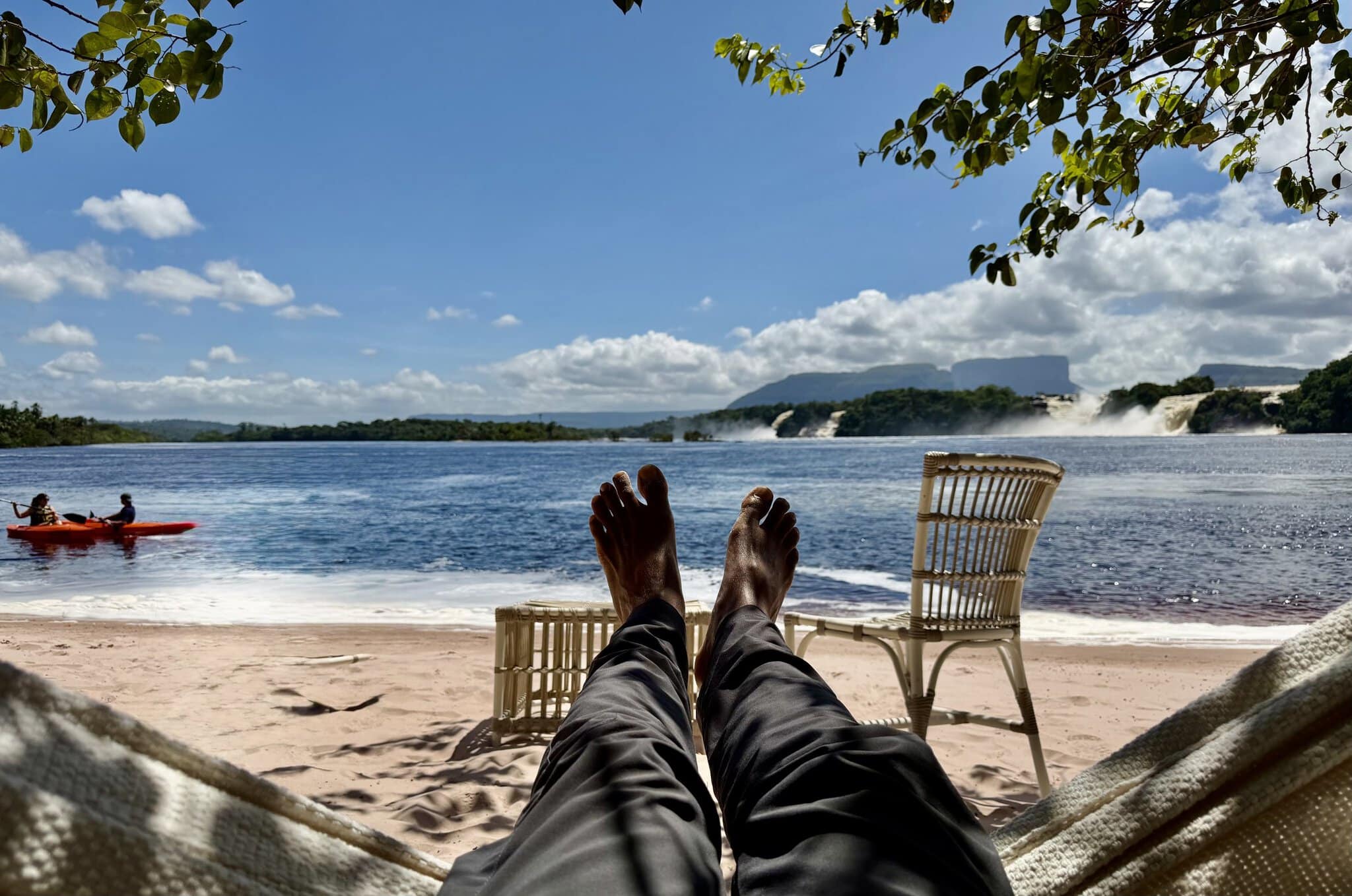 Person relaxing in hammock with feet up overlooking Laguna Canaima with waterfalls and tepui in the distance