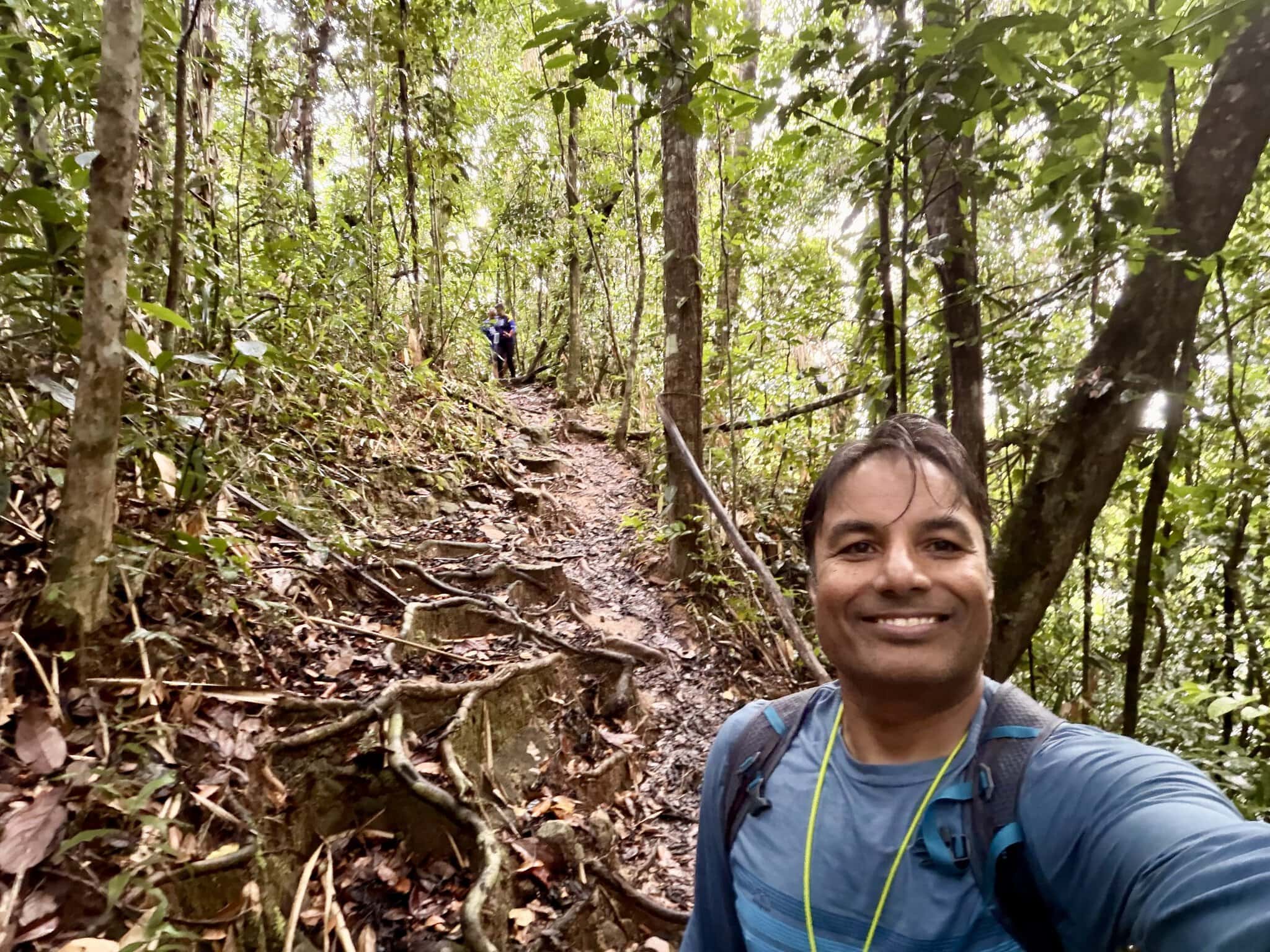 Man taking selfie on muddy jungle trail leading to Angel Falls with lush green rainforest canopy overhead