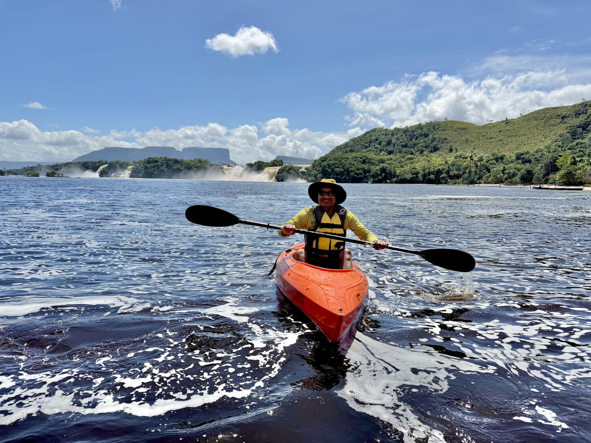 Nirmal kayaking in orange kayak on Canaima Lagoon with waterfalls visible in background