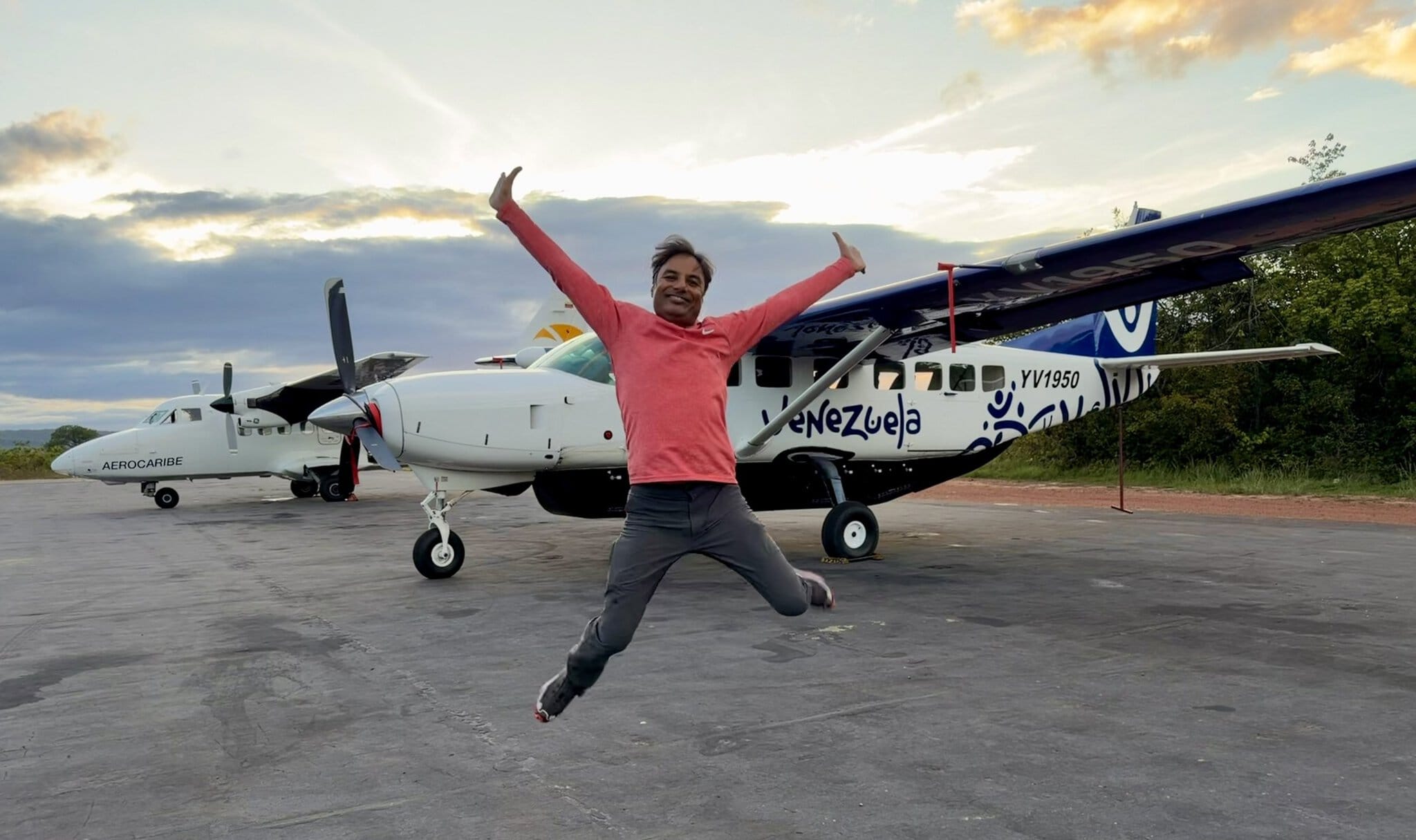 Man jumping joyfully in front of small Venezuela-branded propeller plane on remote airstrip